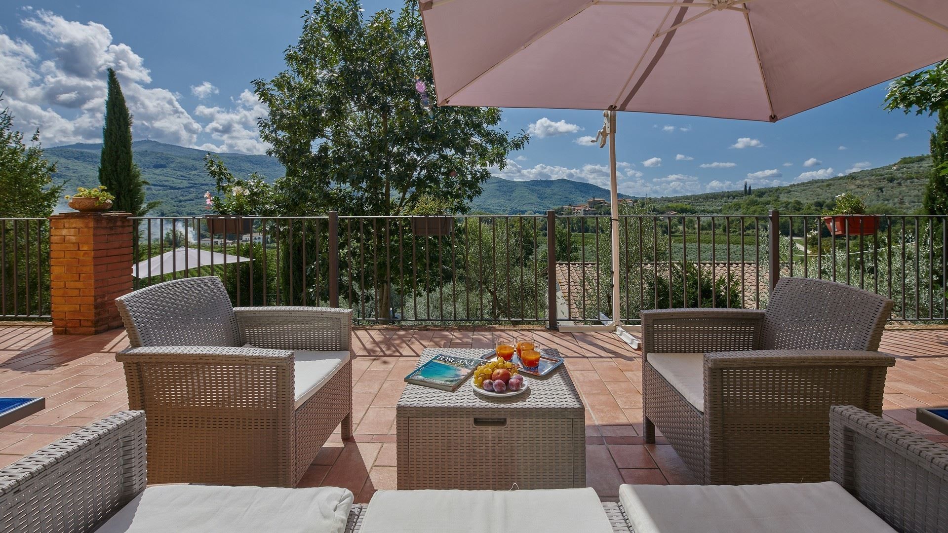 Patio with wicker furniture, food, umbrella, and mountain view on a sunny day.