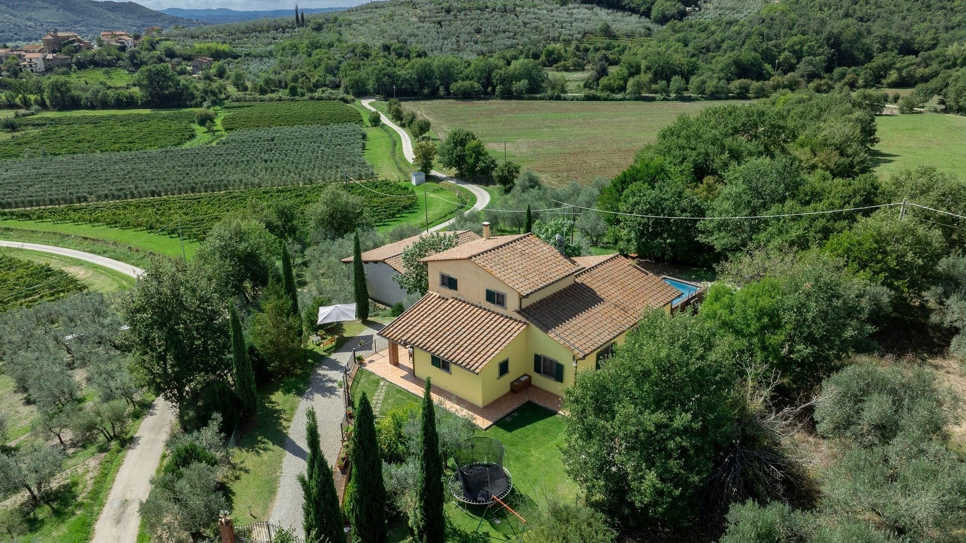 Gelbe Villa in der toskanischen Landschaft mit Olivenhainen und Weinbergen.