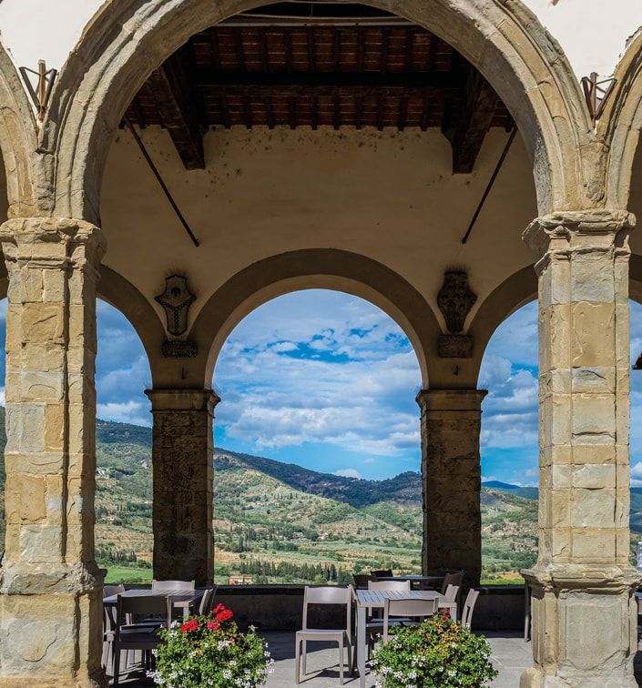 Een stenen boog omlijst het schilderachtige Toscaanse landschap met tafels en stoelen.