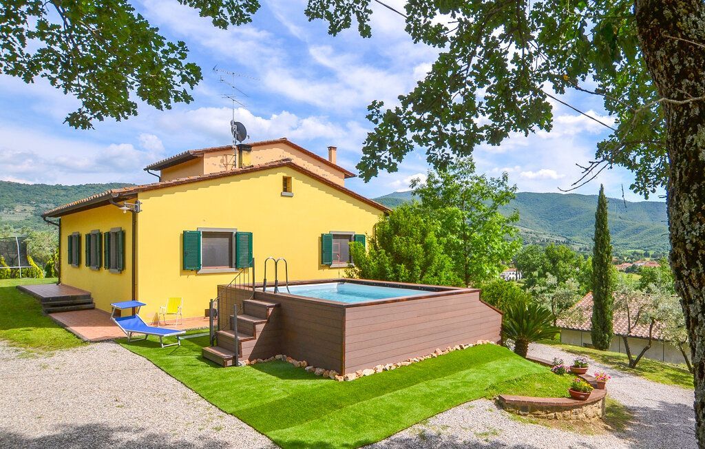 Casa gialla con piscina in un ambiente soleggiato e verdeggiante, con alberi e colline.