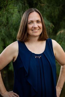 A woman in a blue tank top is standing with her hands on her hips and smiling.