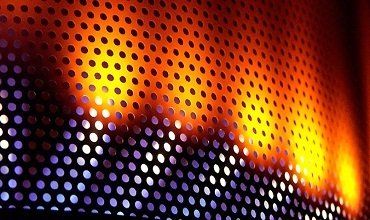 Llamas de color naranja intenso detrás de una pantalla de metal perforado, con un degradado de azul a naranja.