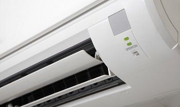 Unidad de aire acondicionado de color blanco, con ventilaciones abiertas y luz verde de “operación”.