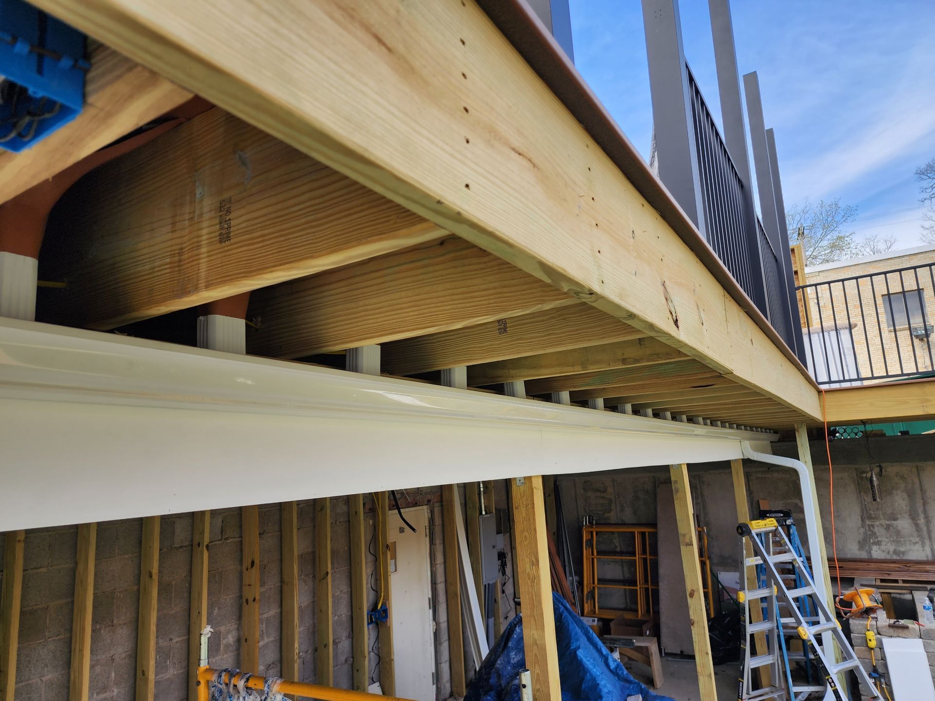 Wooden deck under construction, showing framing and supports, with a metal railing in the background.