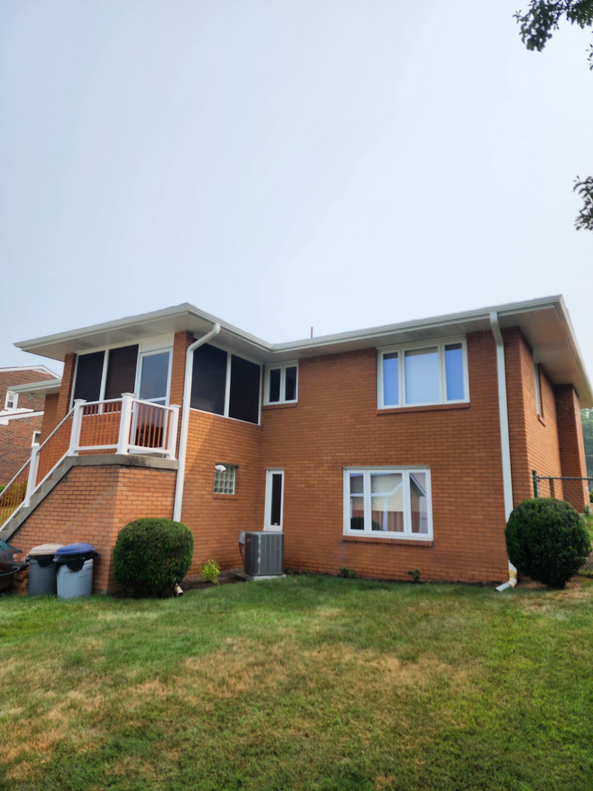 Red brick house with white trim, green lawn, and screened-in porch on a cloudy day.