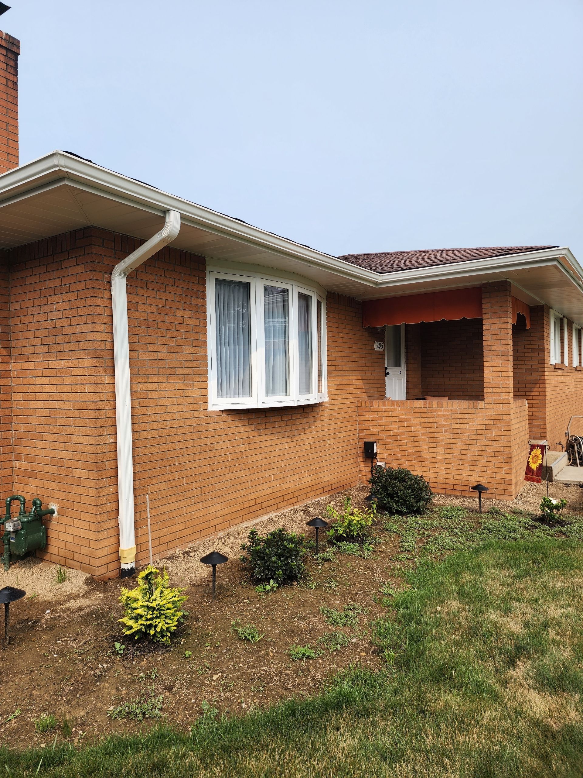 Brick house with white trim, gutters, and a red awning over the doorway. Small bushes and lawn in front.