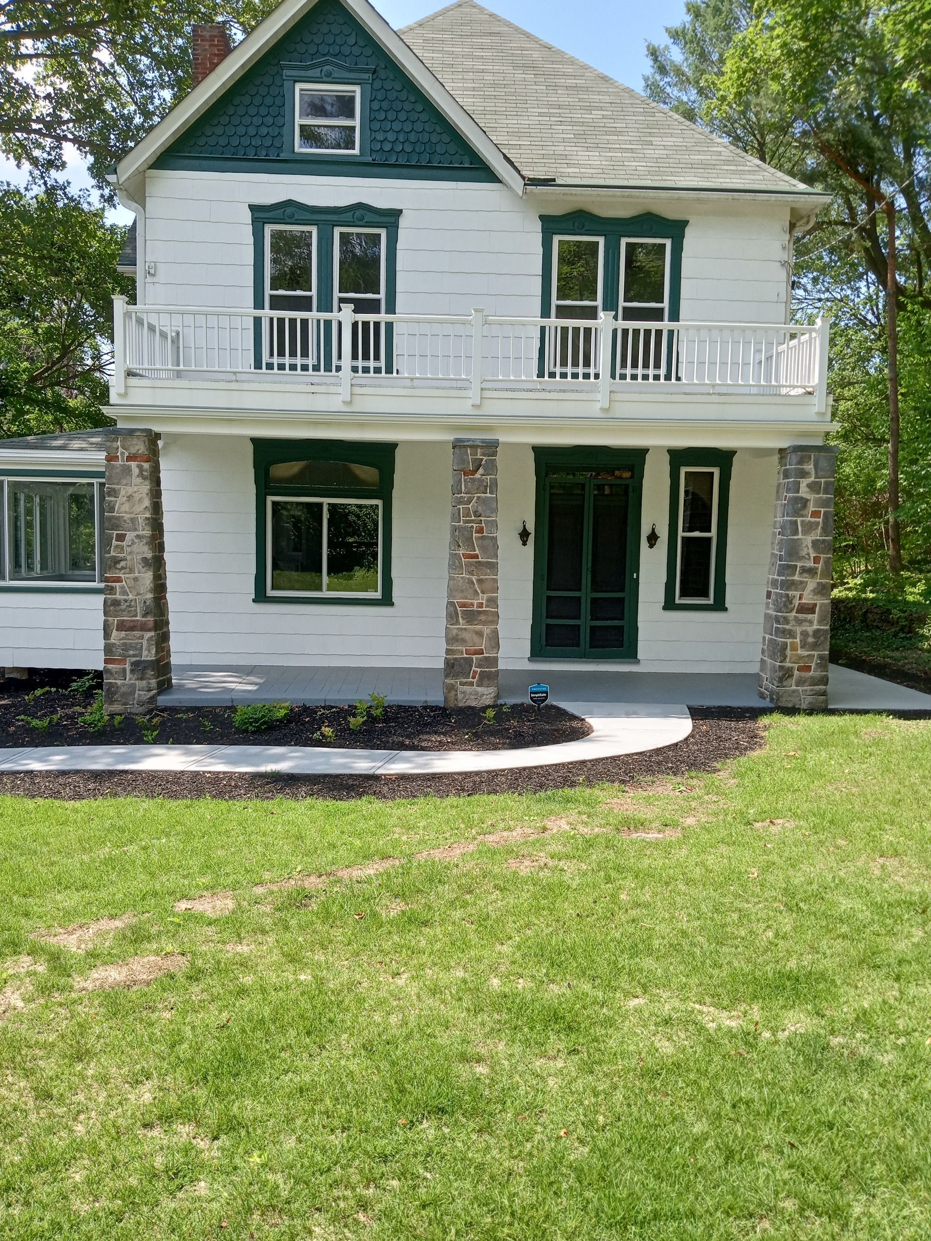 Two-story white house with green trim. Balcony on the second floor supported by stone columns a green door is centered below.