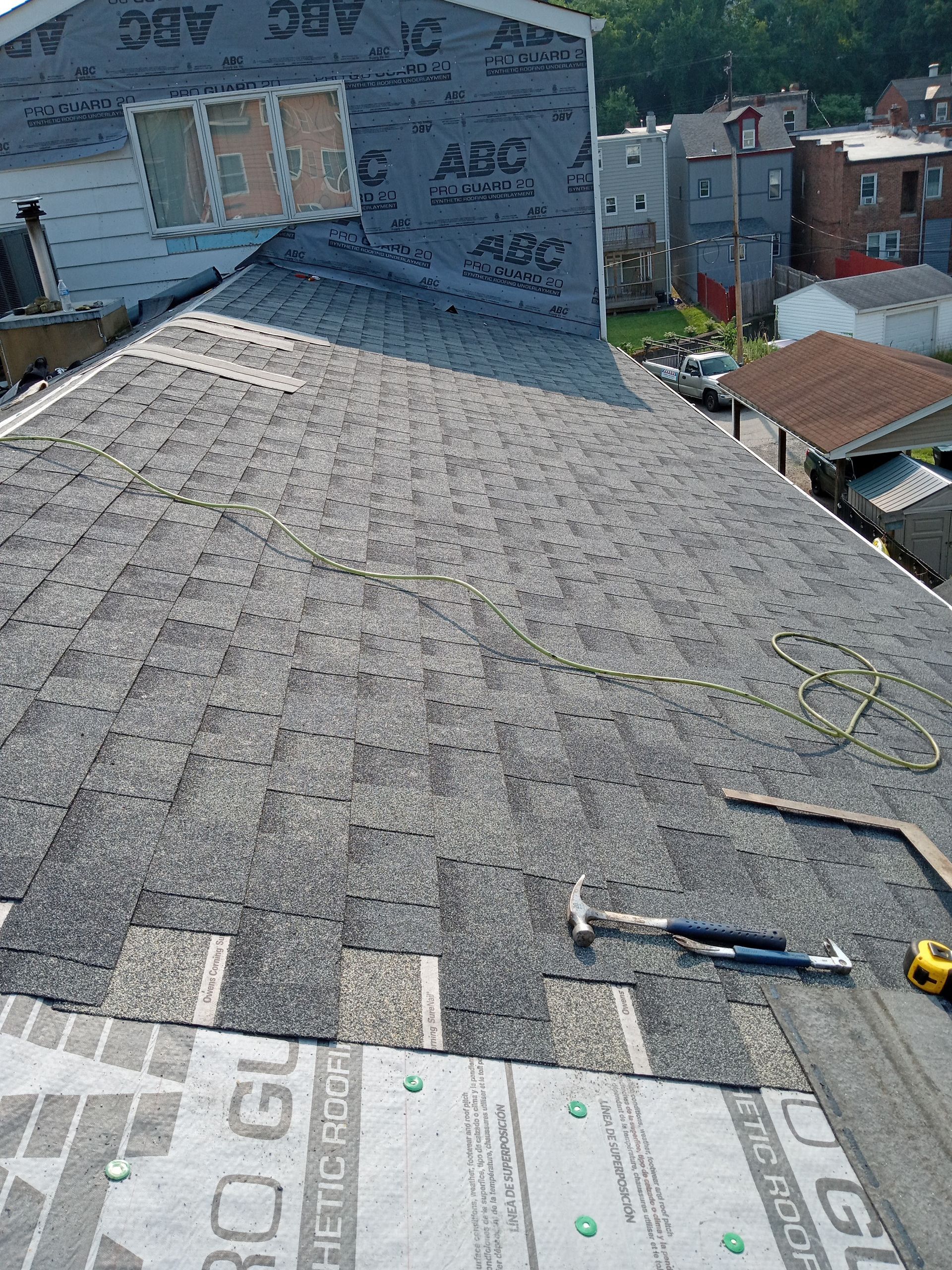 Roofing work in progress; gray shingles, dark underlayment, tools visible, residential setting.