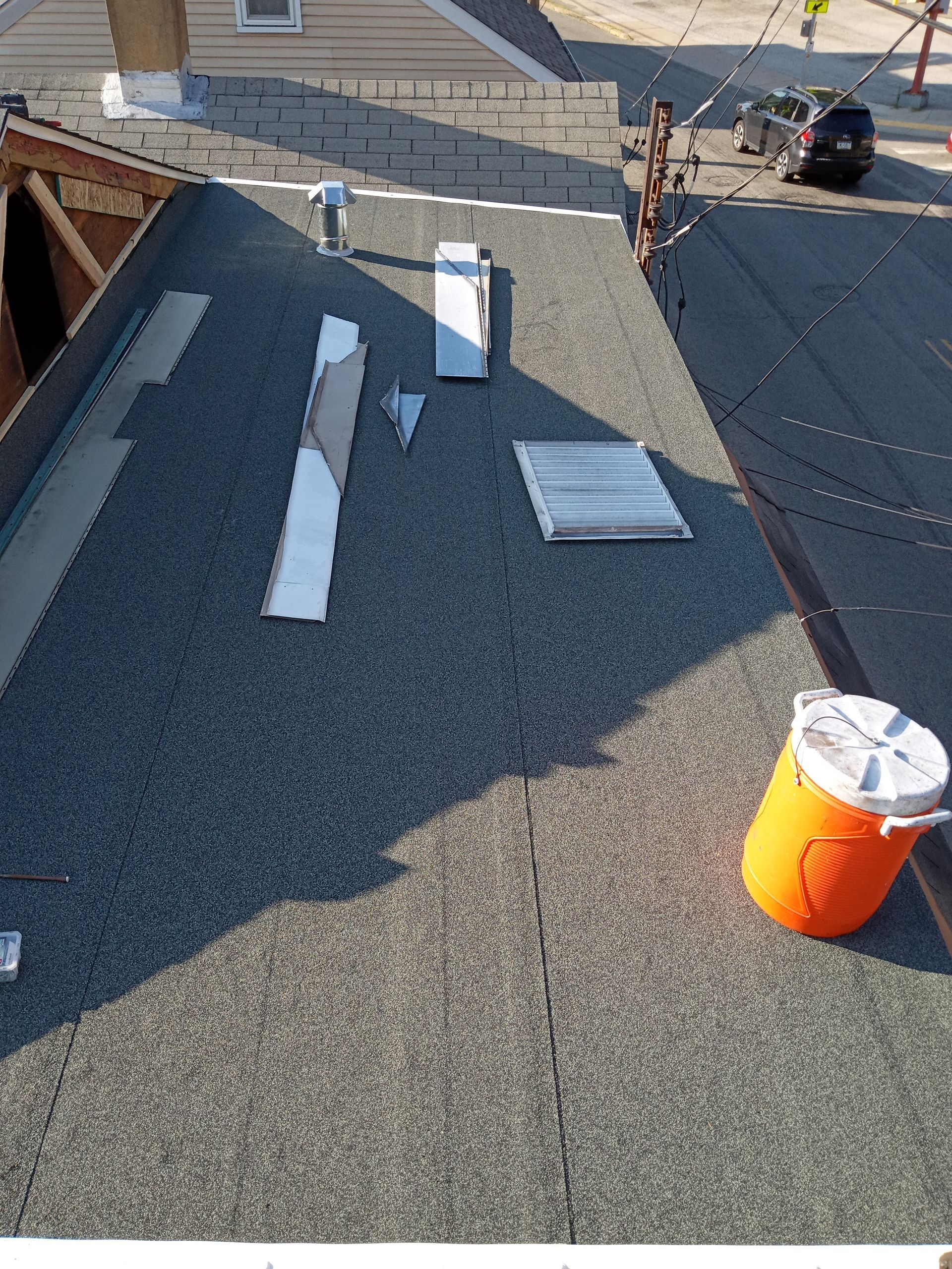 Flat roof with gray and black shingles; an orange cooler, and a person working.