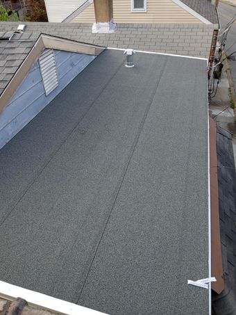 Overhead view of a gray asphalt shingle roof on a house, with a chimney and small vent.