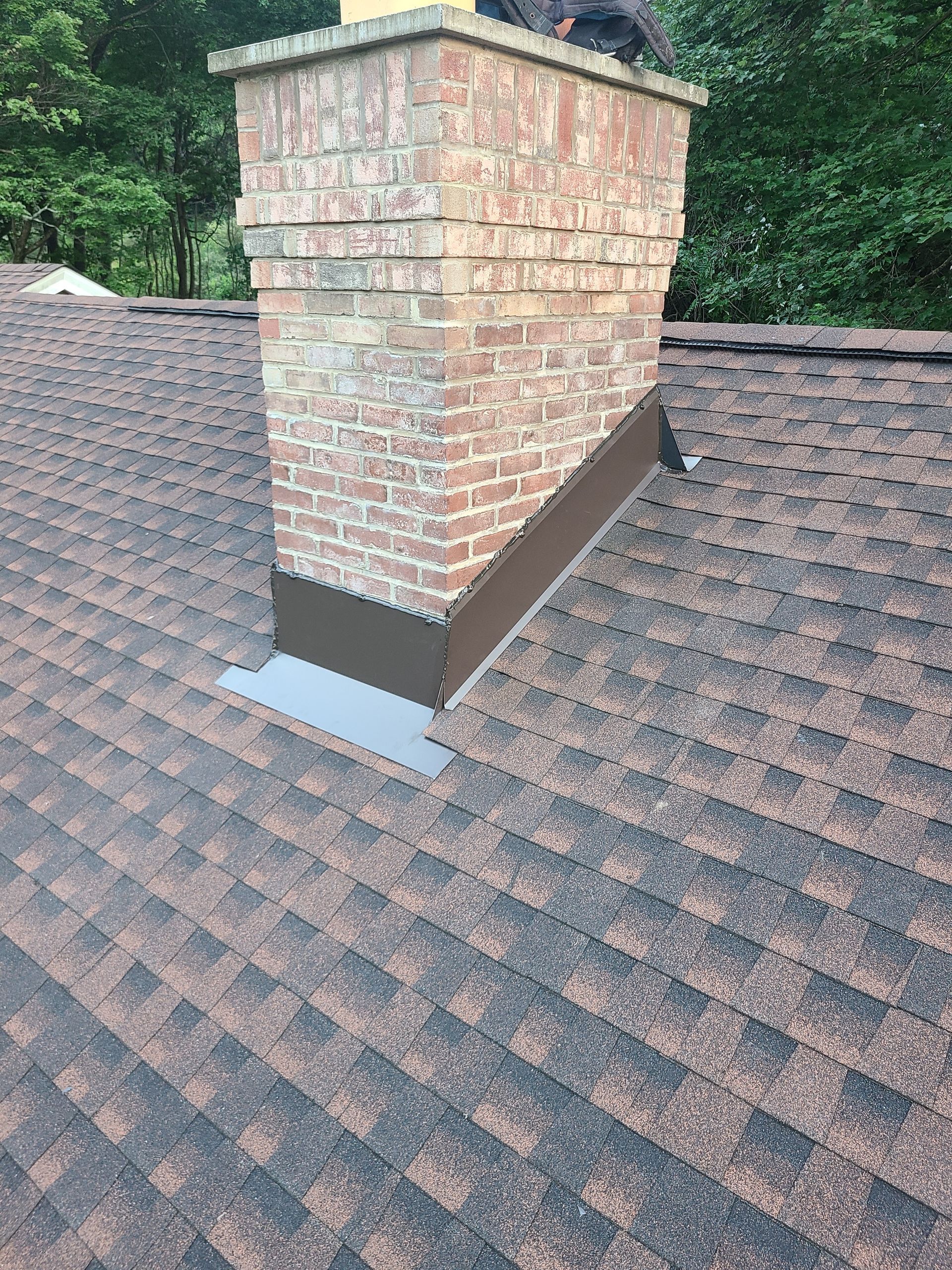 Brick chimney on a brown shingle roof, with metal flashing.