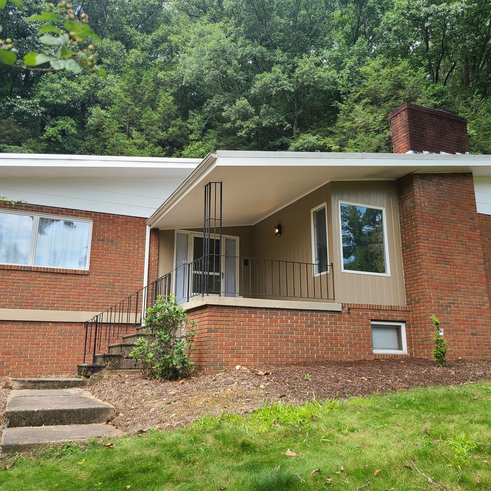 Brick home with porch and steps, surrounded by grass and trees.