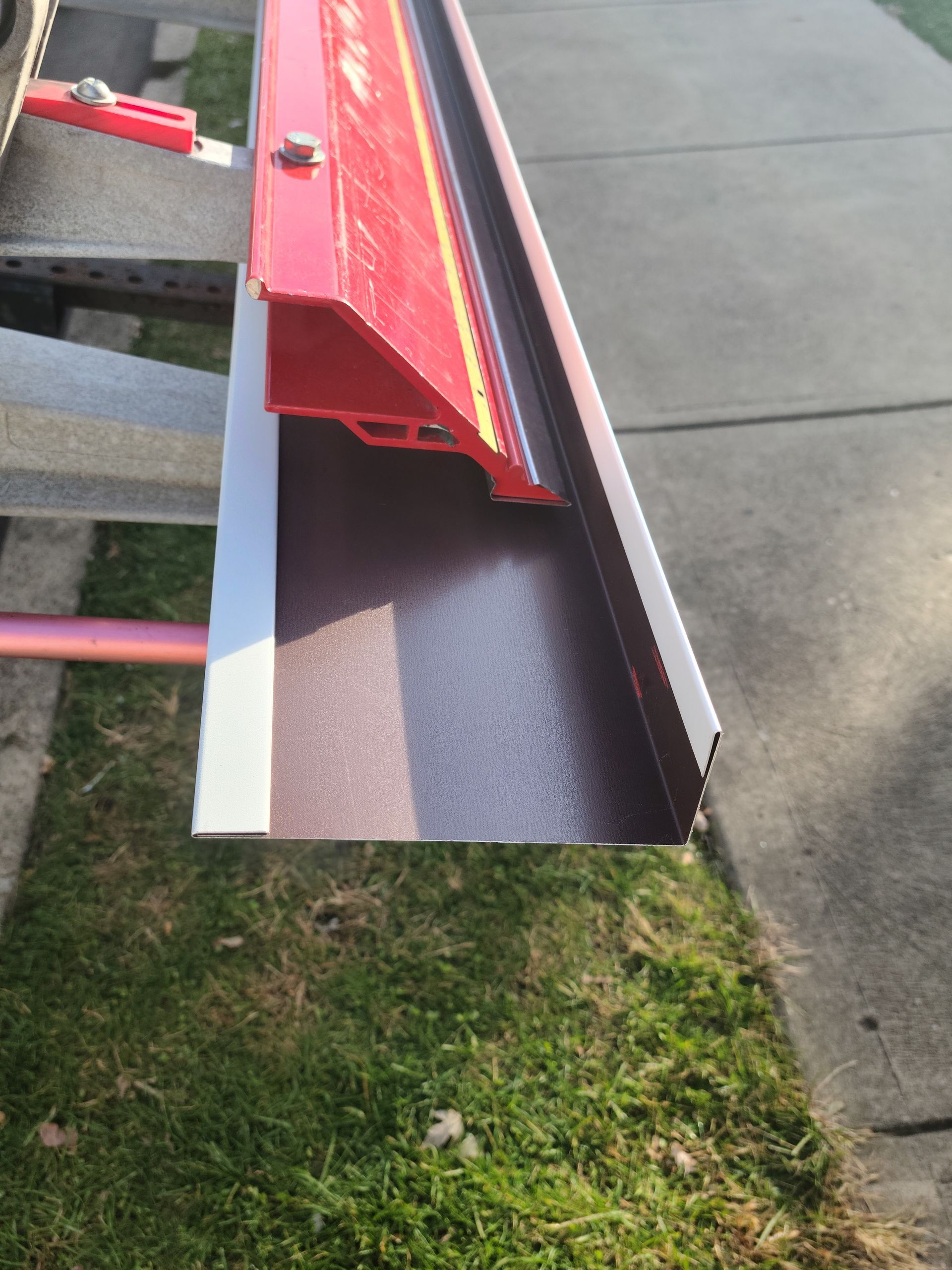 Corner of a house with light siding and a gutter against a blue sky.