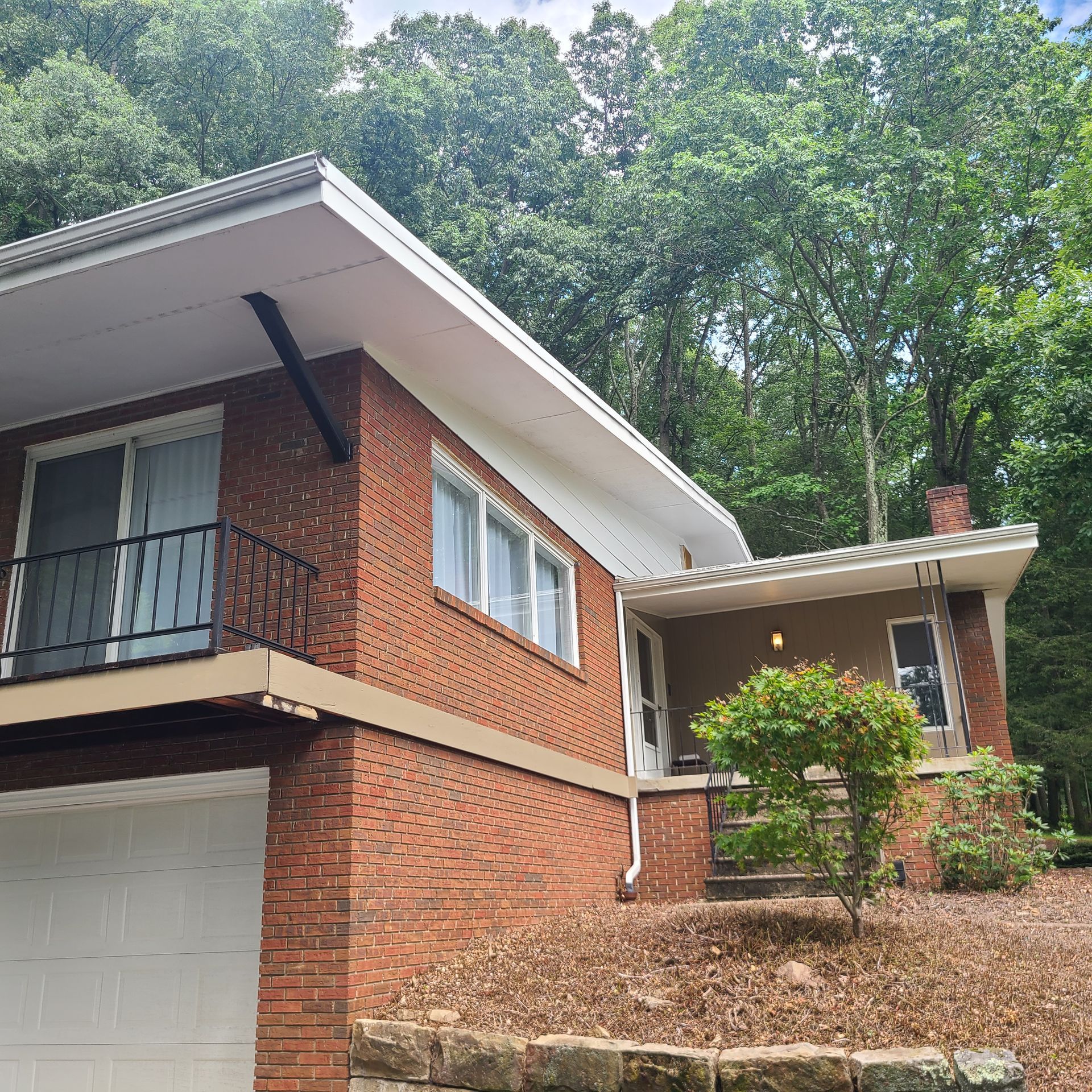 Brick house with white trim, black balcony, and trees.