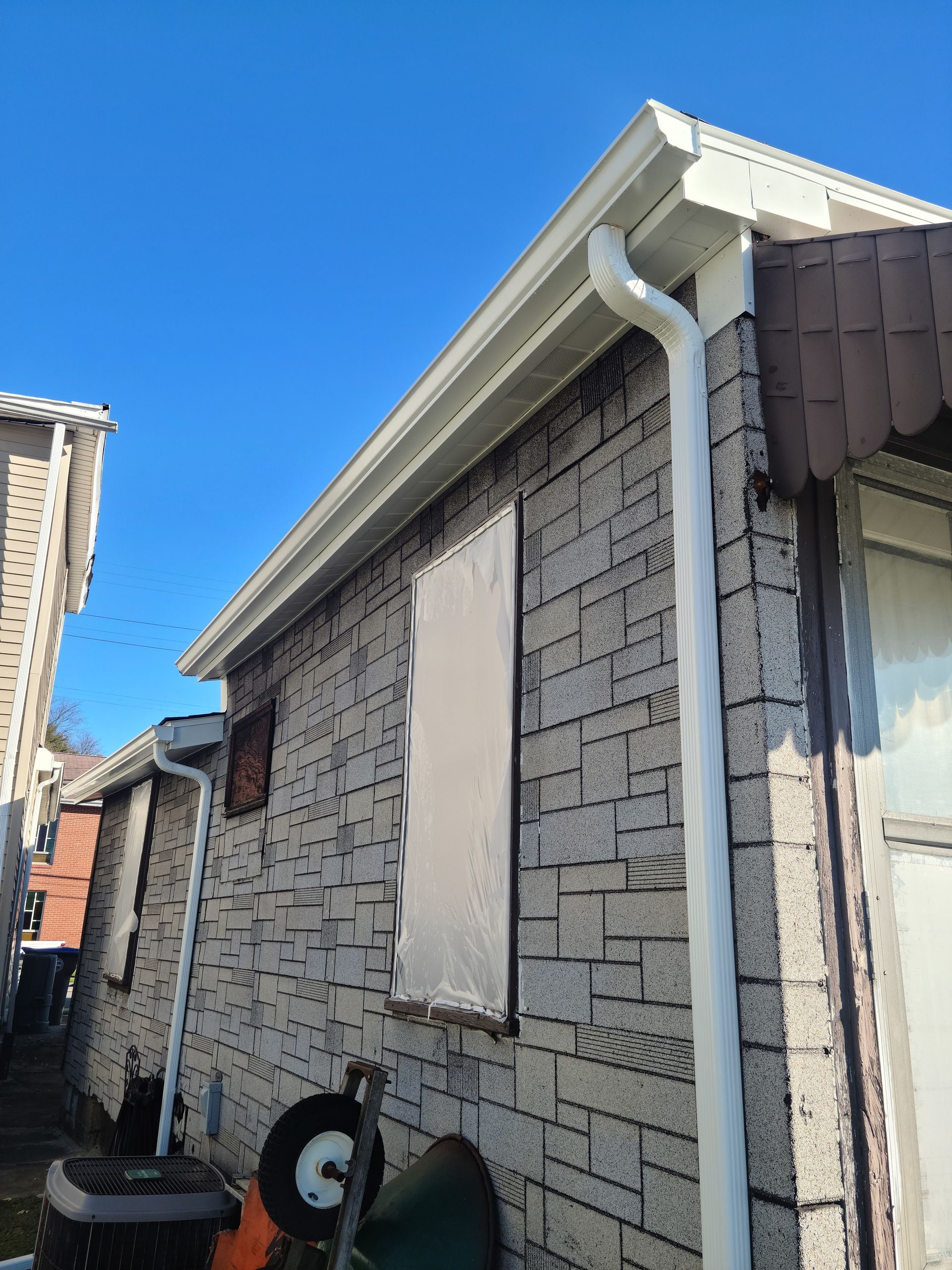 Exterior of a brick building with white gutters and a boarded-up window under a clear blue sky.