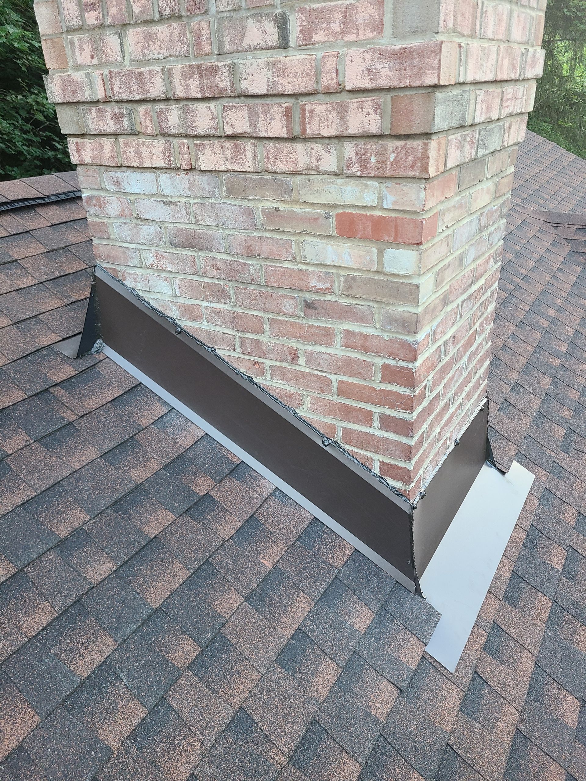 Brick chimney with brown metal flashing on a shingled roof.
