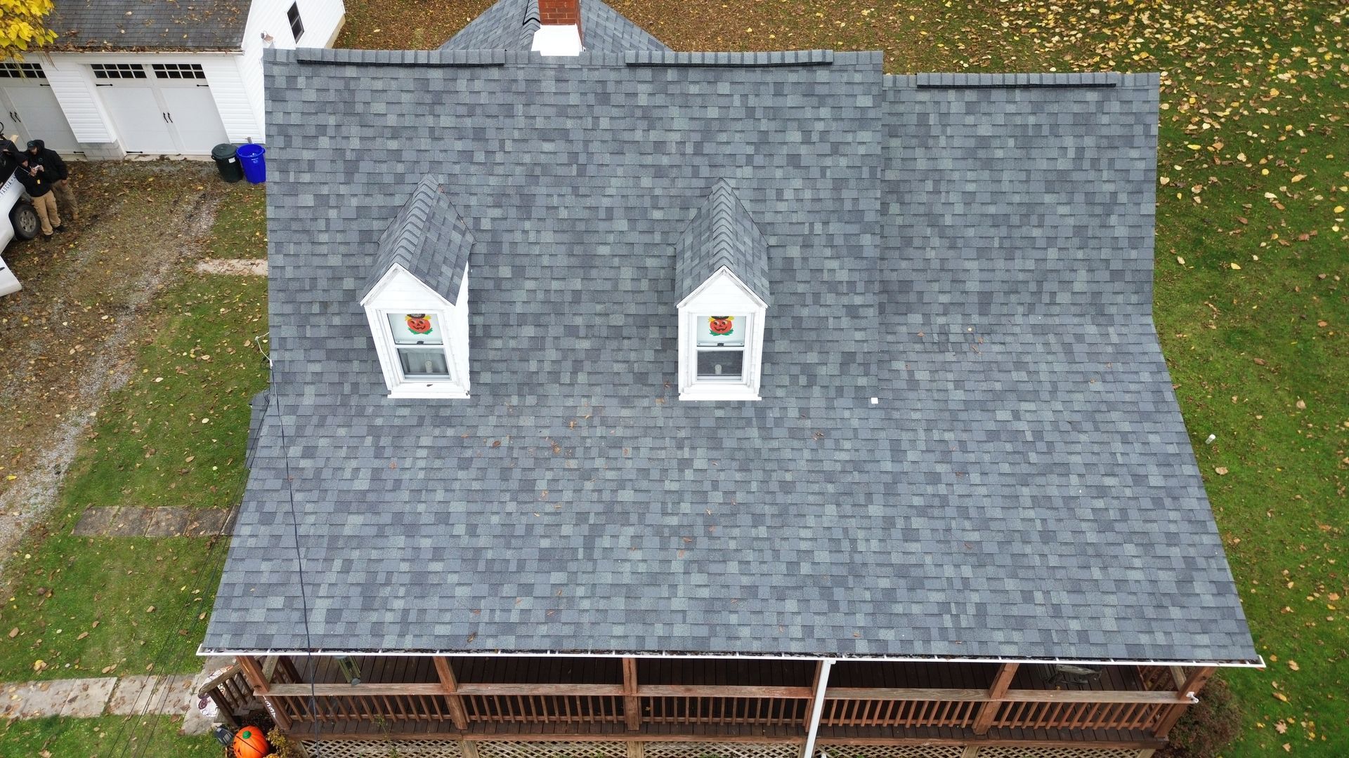 Overhead view of a house with a gray shingled roof, two dormers, and a wooden porch.