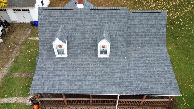 Overhead view of a house with a gray shingled roof, two dormers, and a wooden porch.