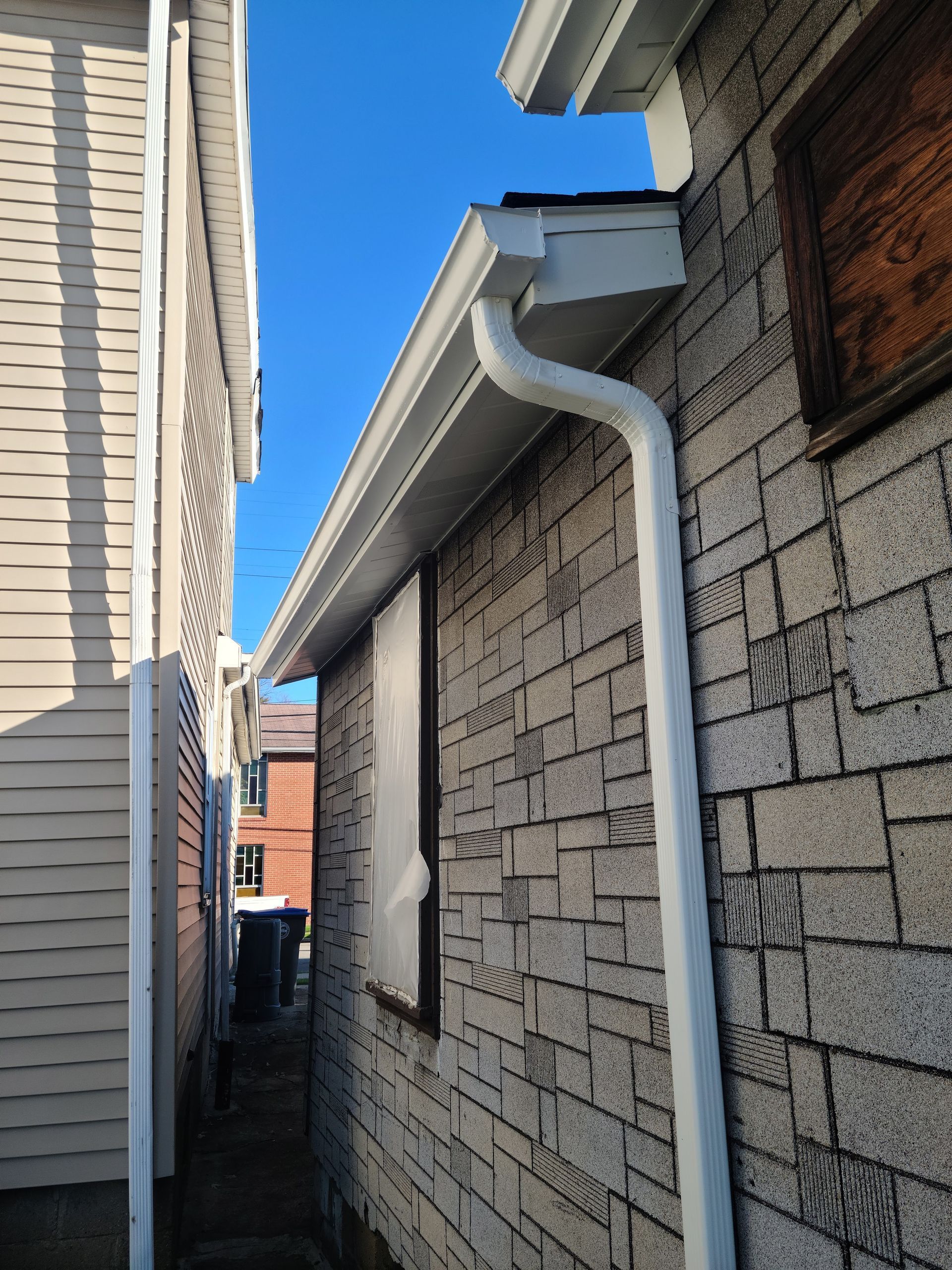 White gutters and downspout on a brick building with a vinyl-sided building next door.