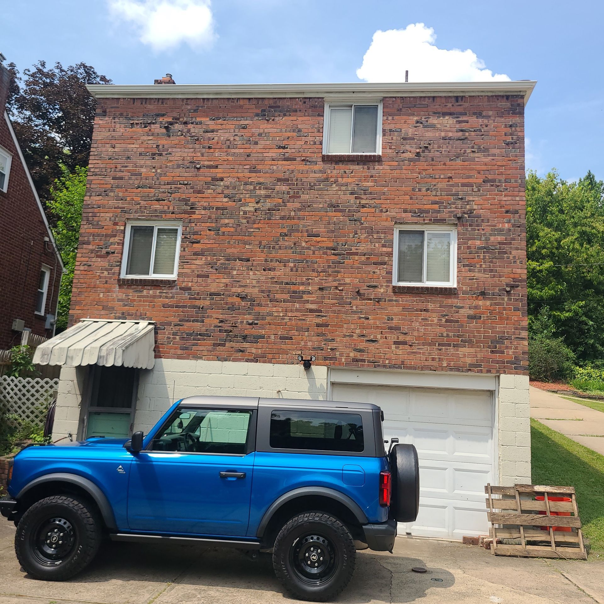 Blue Ford Bronco parked in front of a brick building with a garage, windows, and awning.