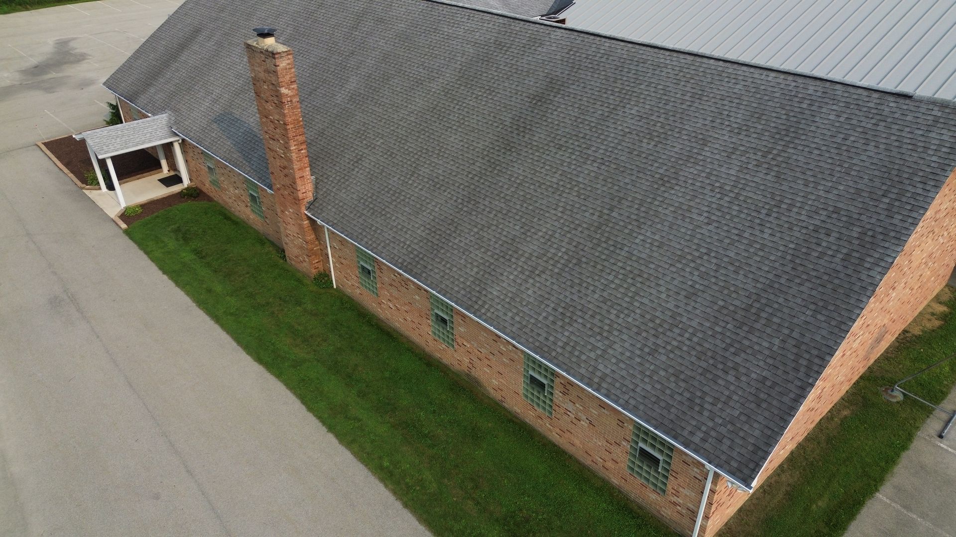 Brick building with gray roof, chimney, green lawn, and asphalt.