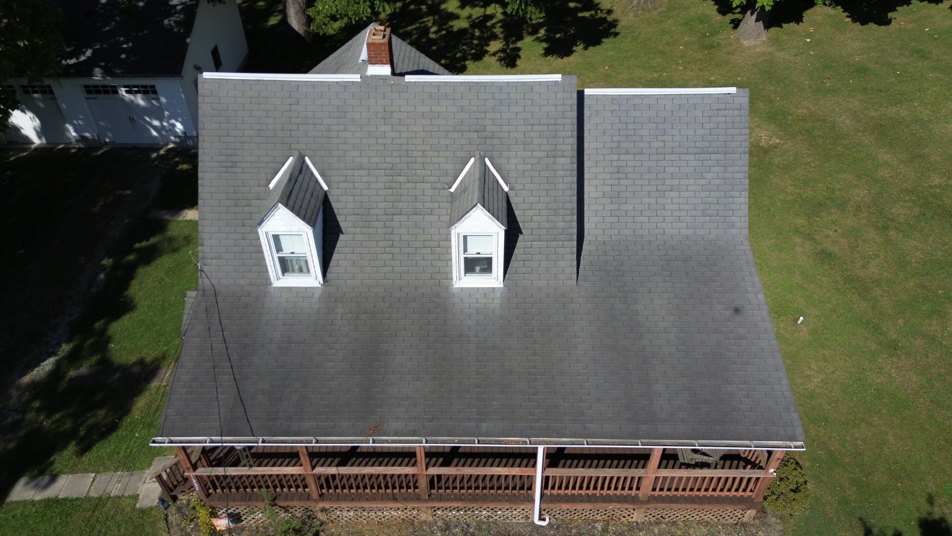 Overhead view of a house with a gray shingle roof, two dormers, and a brown wooden porch.
