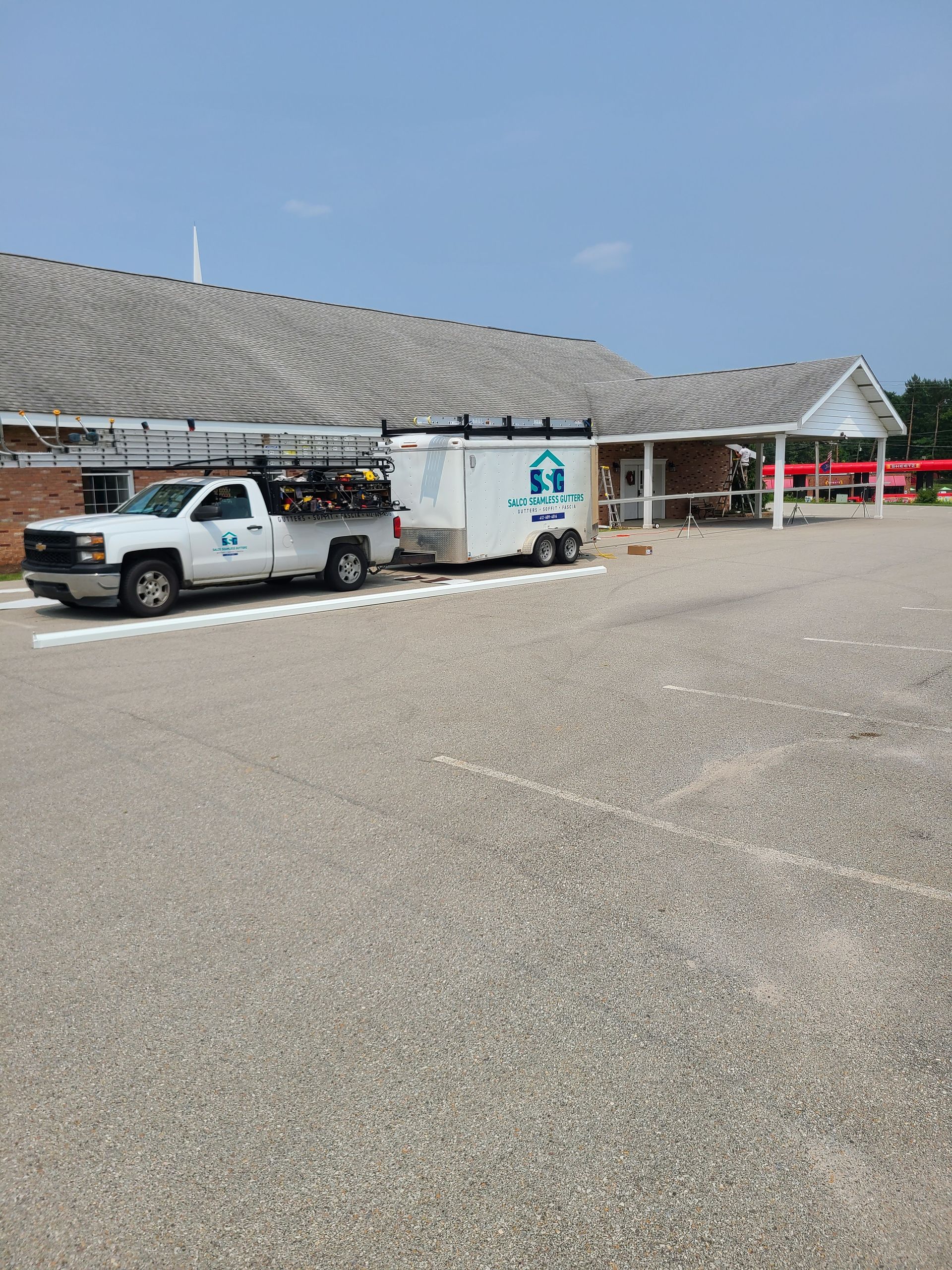 White truck pulling a trailer in a gravel parking lot by a brick building with a covered entrance.