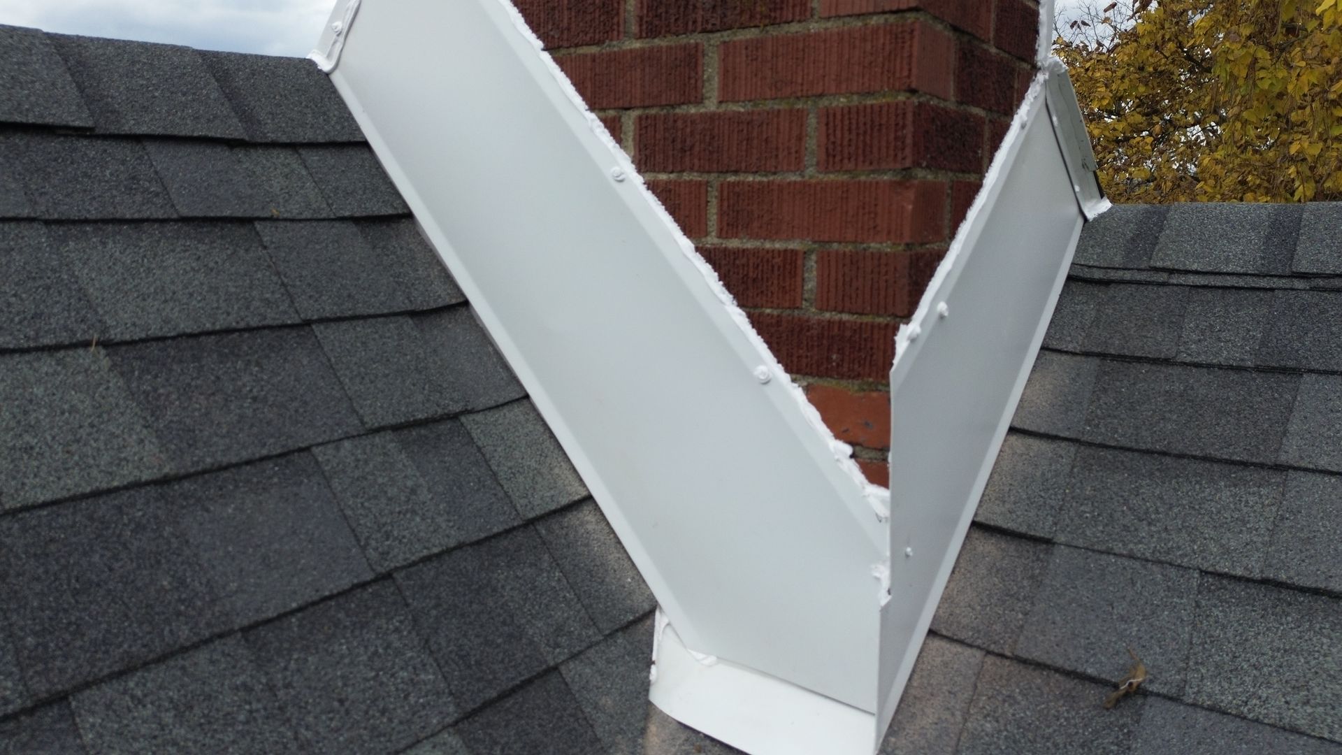 White flashing around a brick chimney on a gray shingled roof.