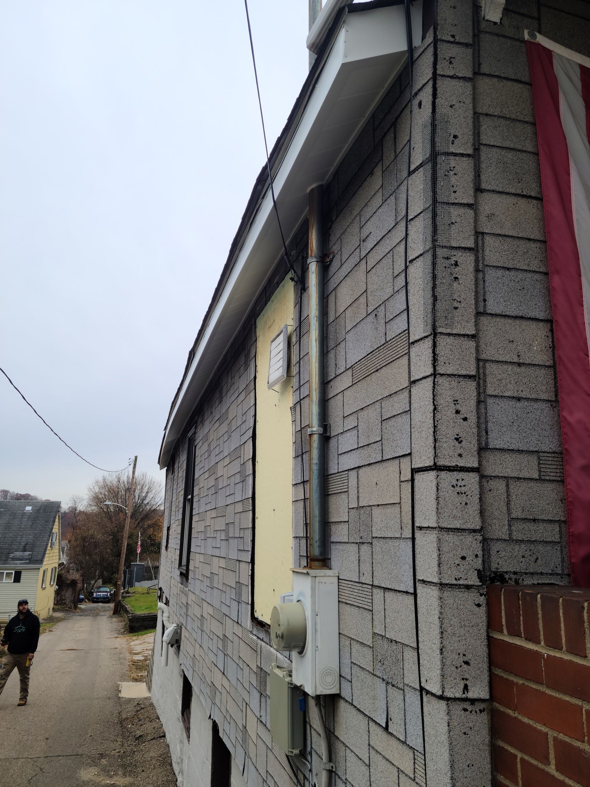 Gray shingle roof with white gutters and a downspout, against a green background.