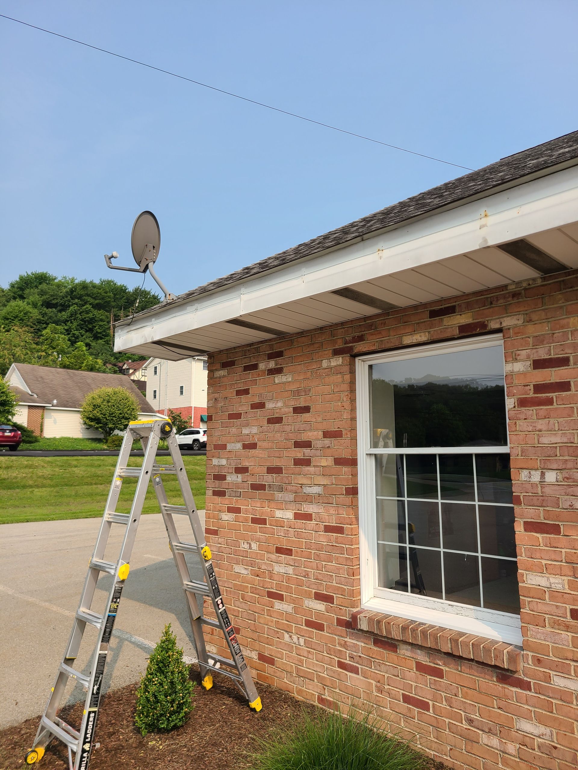 Black metal roof on a brick house against a blue sky with clouds.
