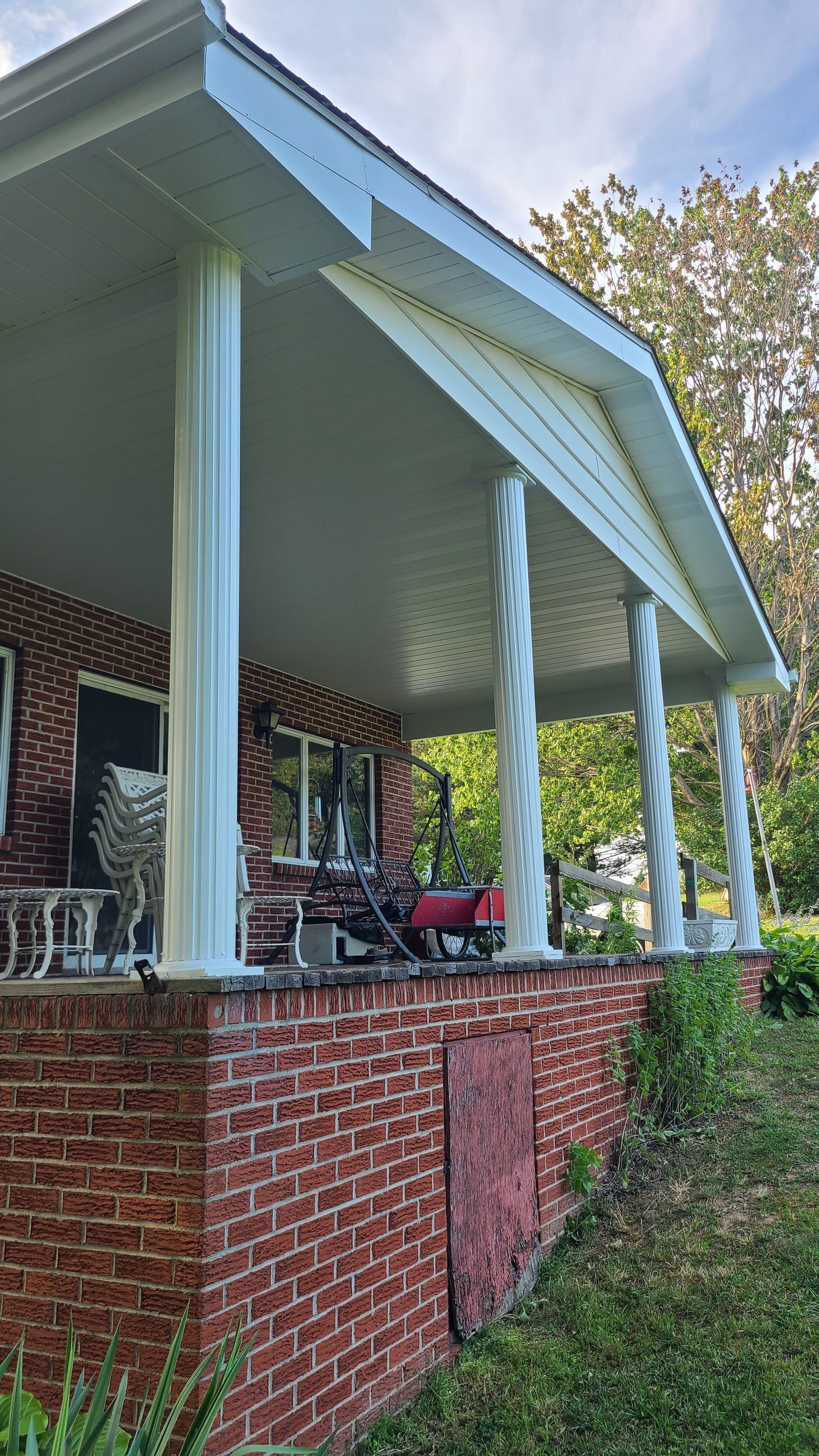 Brick house with white columns supporting a porch roof, and a red brick foundation.