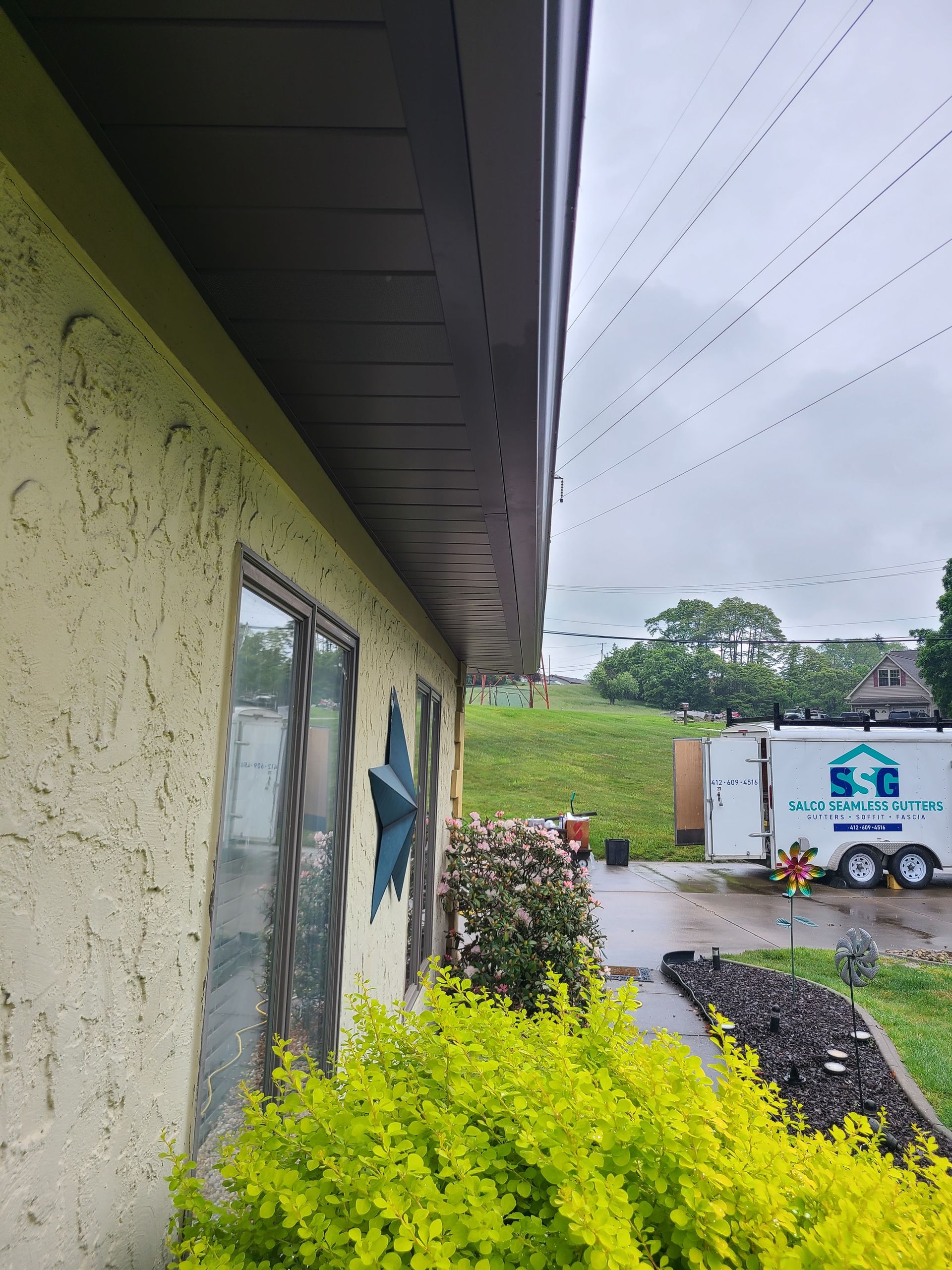 Yellow house with brown trim and dark gutters, cloudy day.