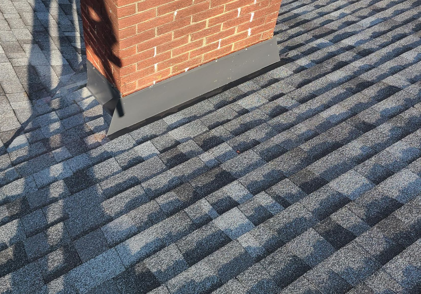 Brick chimney with black flashing on a gray shingled roof.