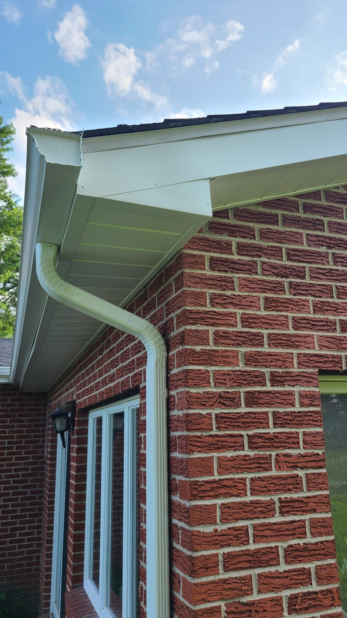 Brick house corner with white gutters and trim under a blue sky.