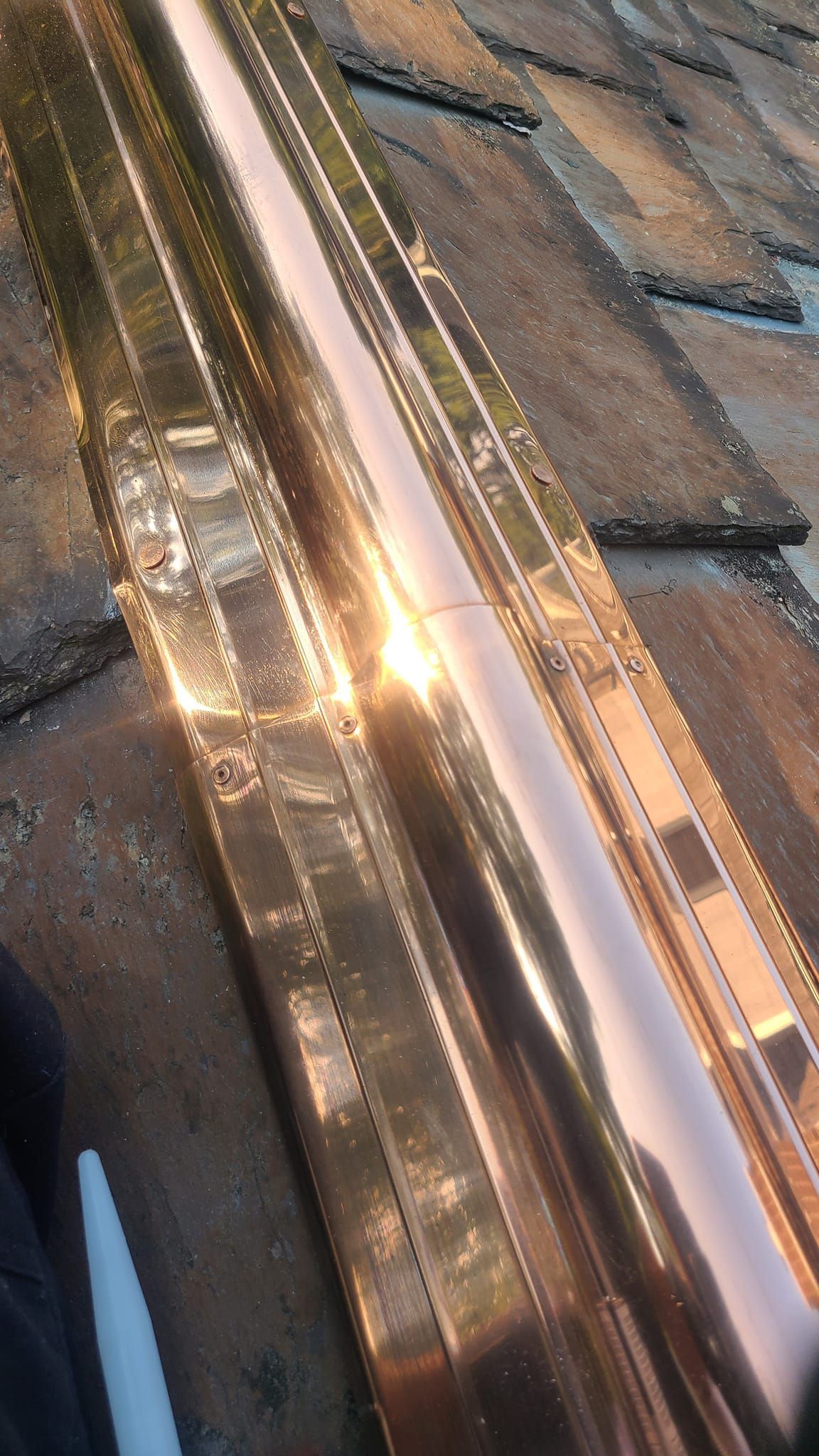 Copper flashing installed on a roof with dark gray shingles reflecting sunlight.