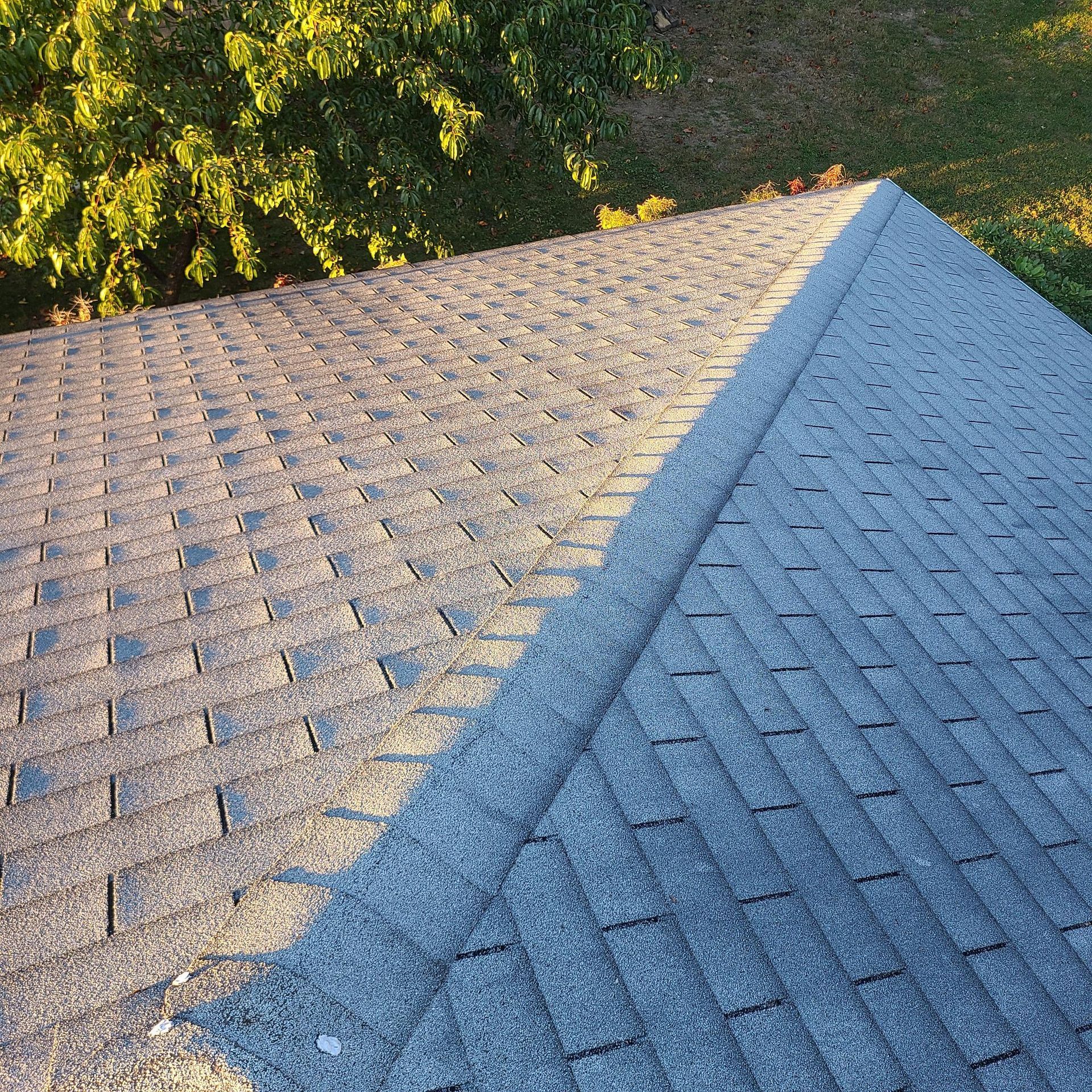 Gray asphalt shingle roof, with a ridge line and sunlight casting a shadow.