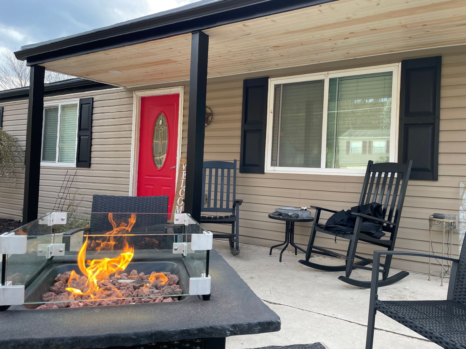 A front porch with a fire pit, red door, and rocking chairs.