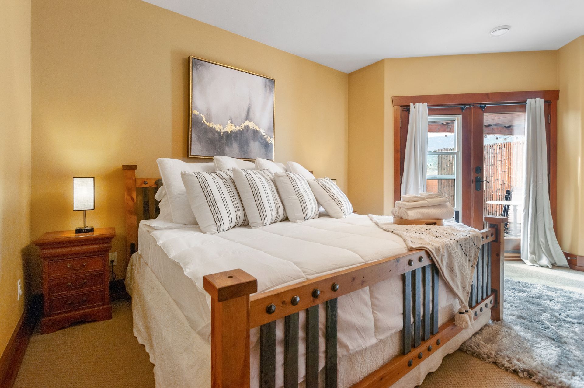 A bedroom with a king size bed , nightstand , lamp and sliding glass doors.