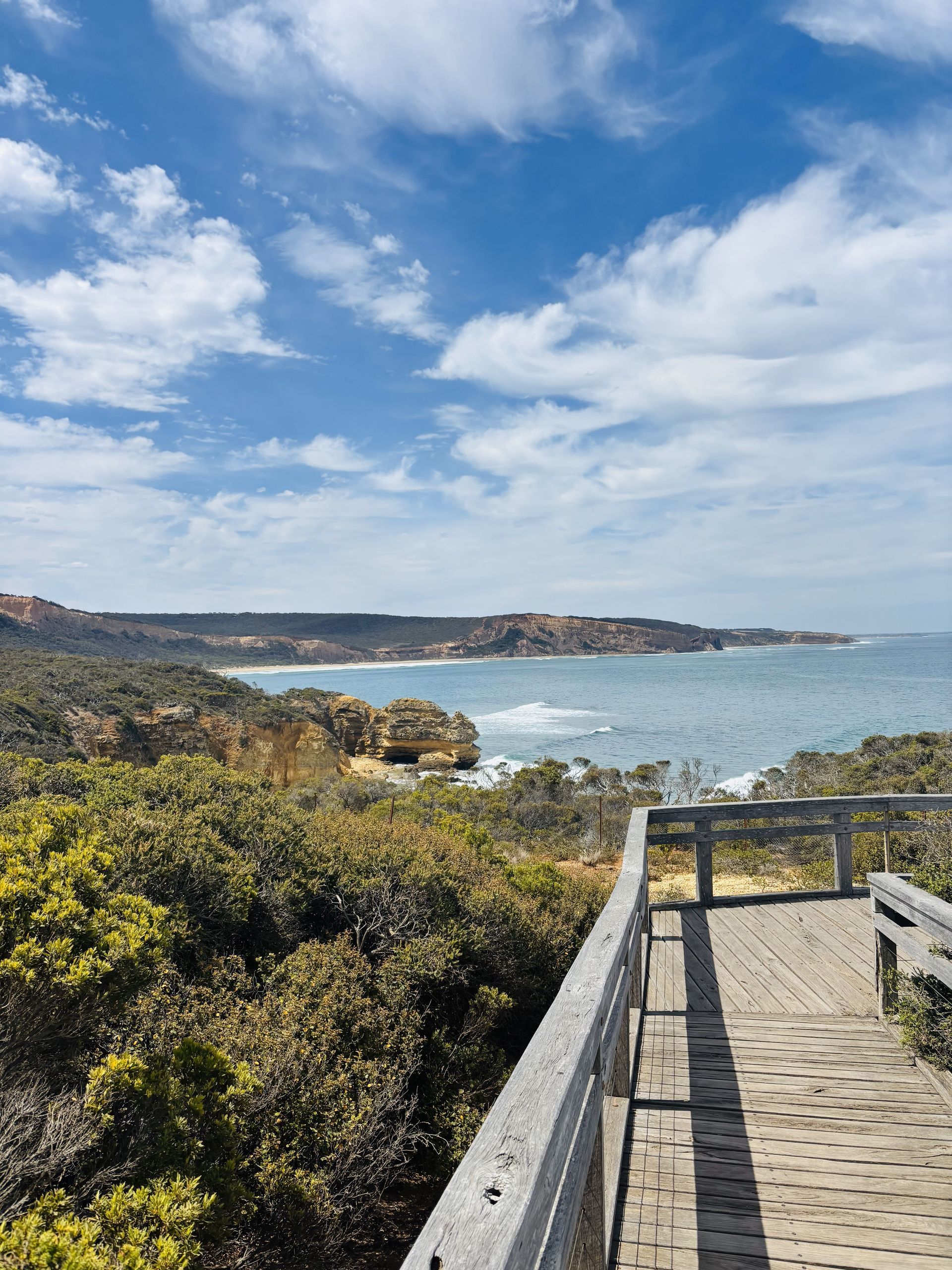 Wooden boardwalk overlooking the ocean, blue sky with clouds. Coastal landscape with vegetation.