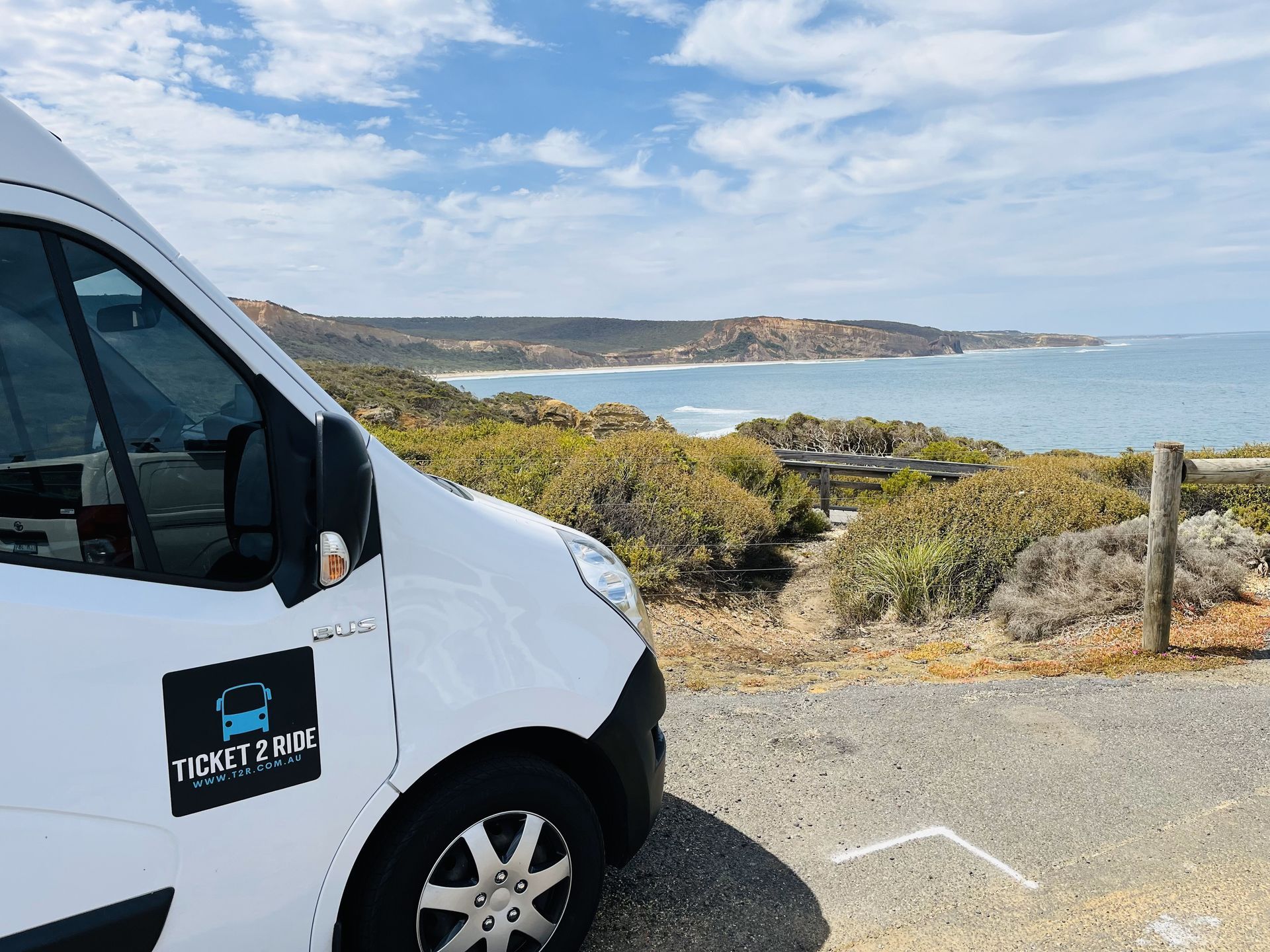 White Ticket 2 Ride minibus parked overlooking a coastal view; ocean, brush and hills.