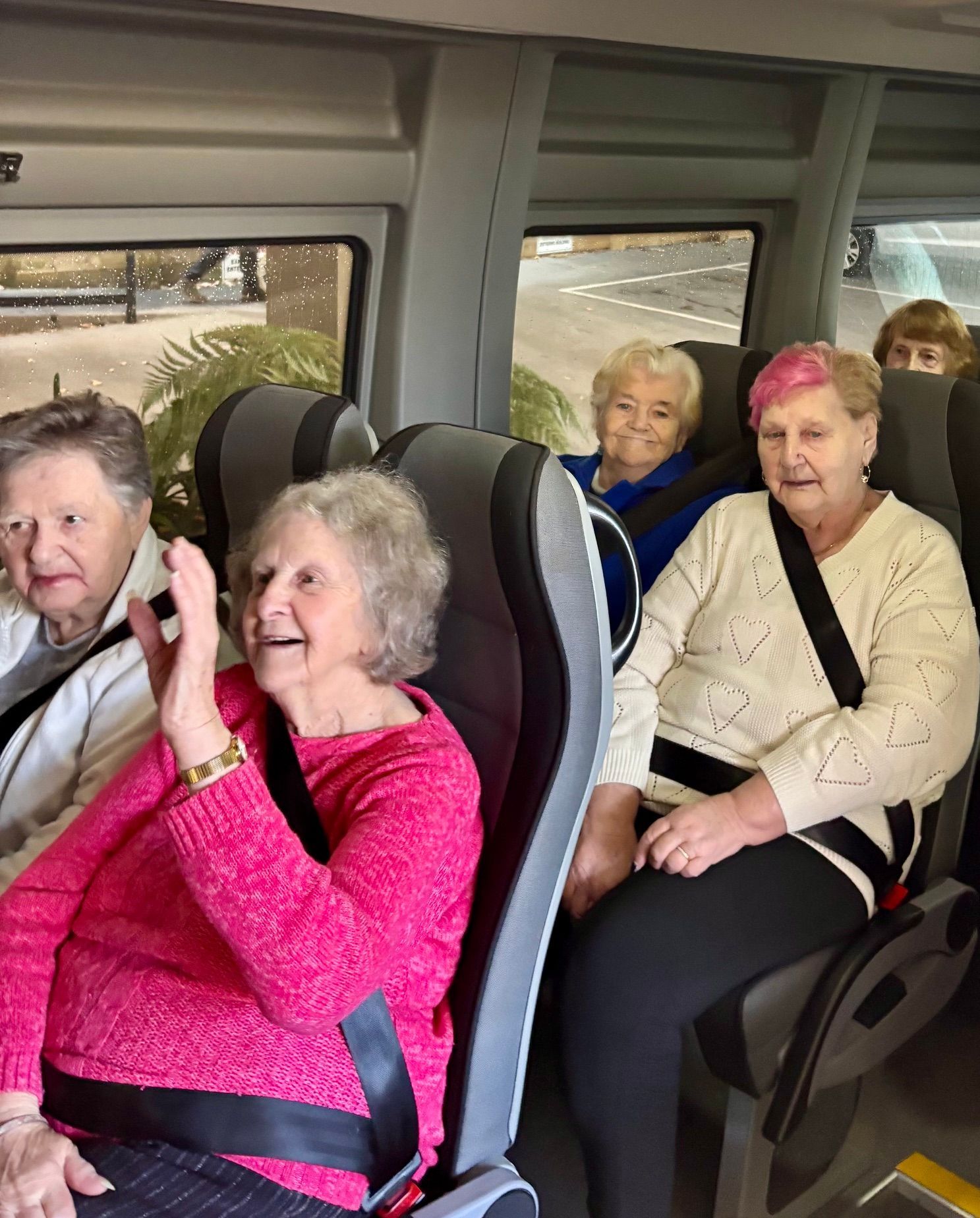 People in a Ticket 2 Ride minibus, some smiling, waving, and wearing sunglasses, enjoying a trip together.
