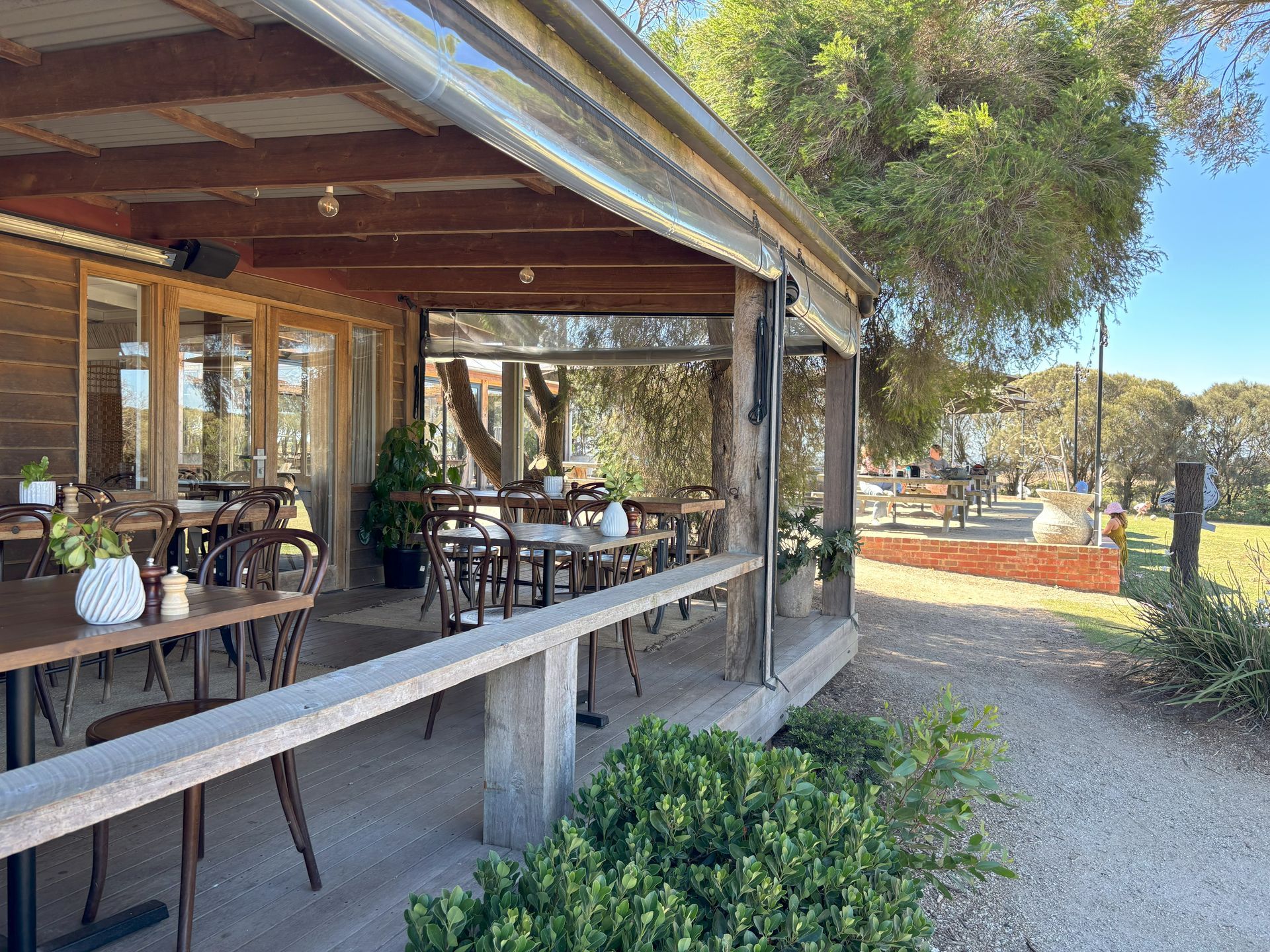 Undercover winery seating with wooden tables and chairs on a covered porch with views of a grassy area and trees.