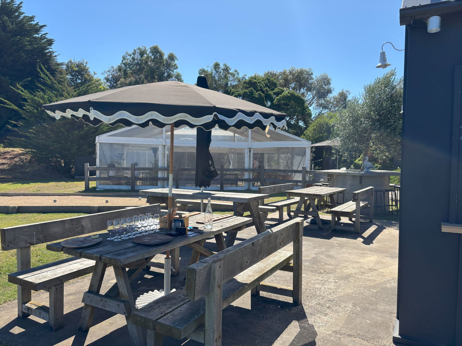 Outdoor seating area with picnic tables, a black and white umbrella, and a white event tent.