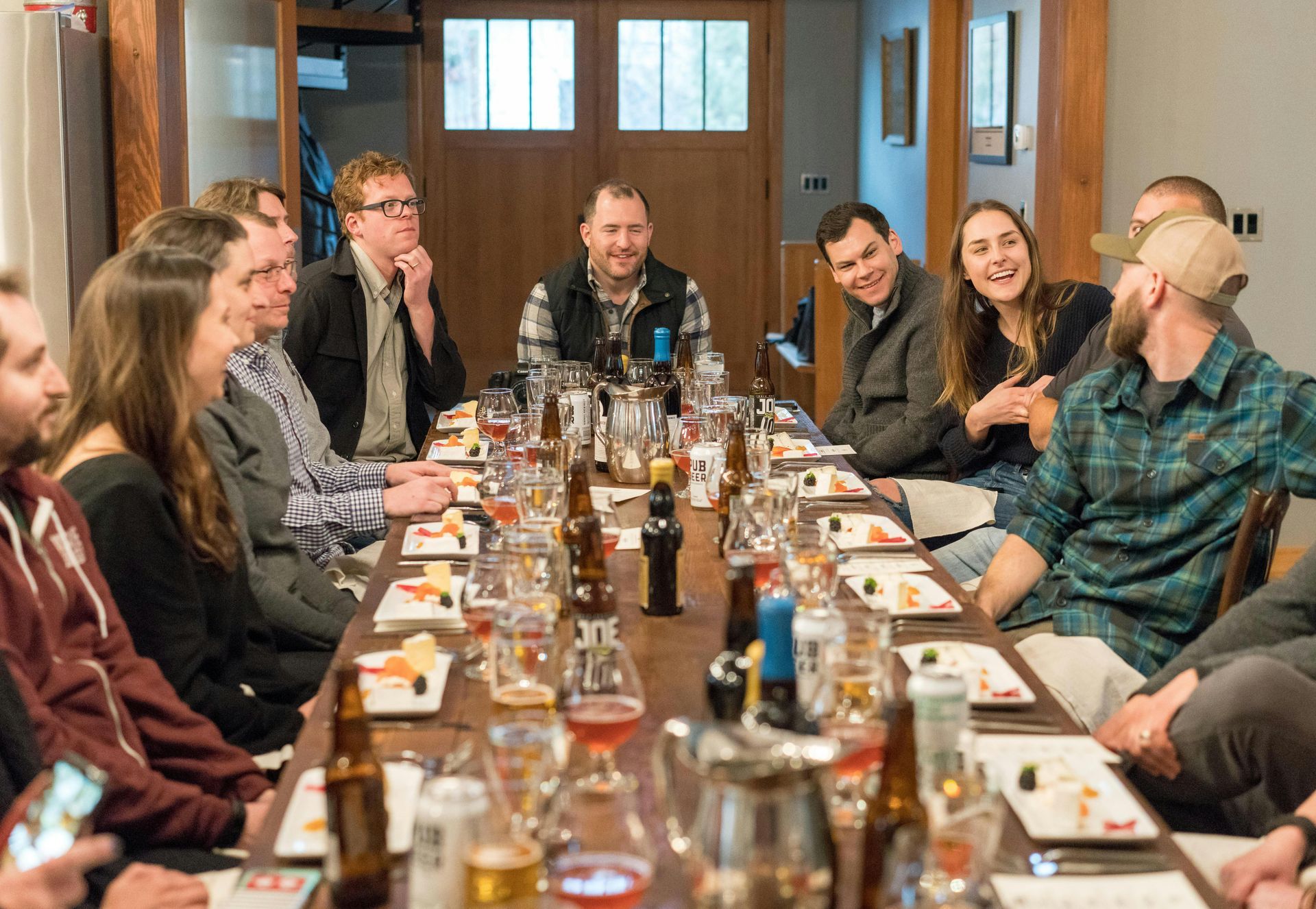 People at a long table, enjoying a meal and drinks. Laughter and conversation in a warmly lit room.