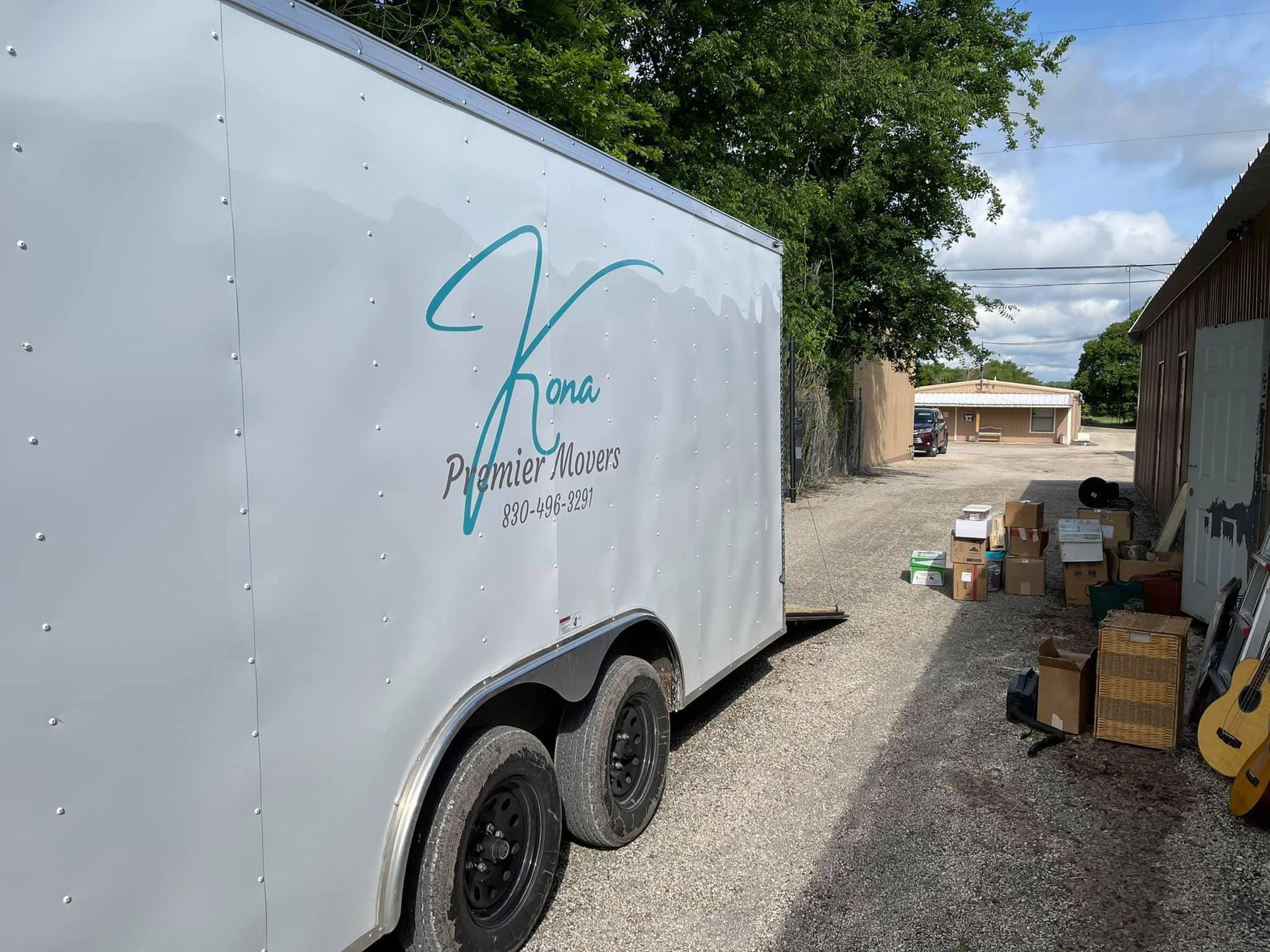 A white trailer is parked in a gravel lot next to a building.