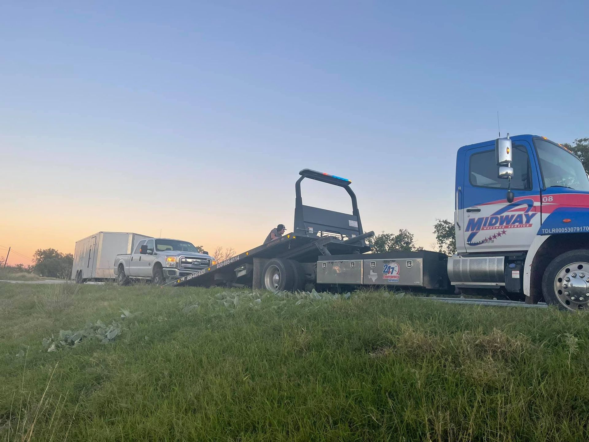 A tow truck with a trailer attached to it is parked in a grassy field.