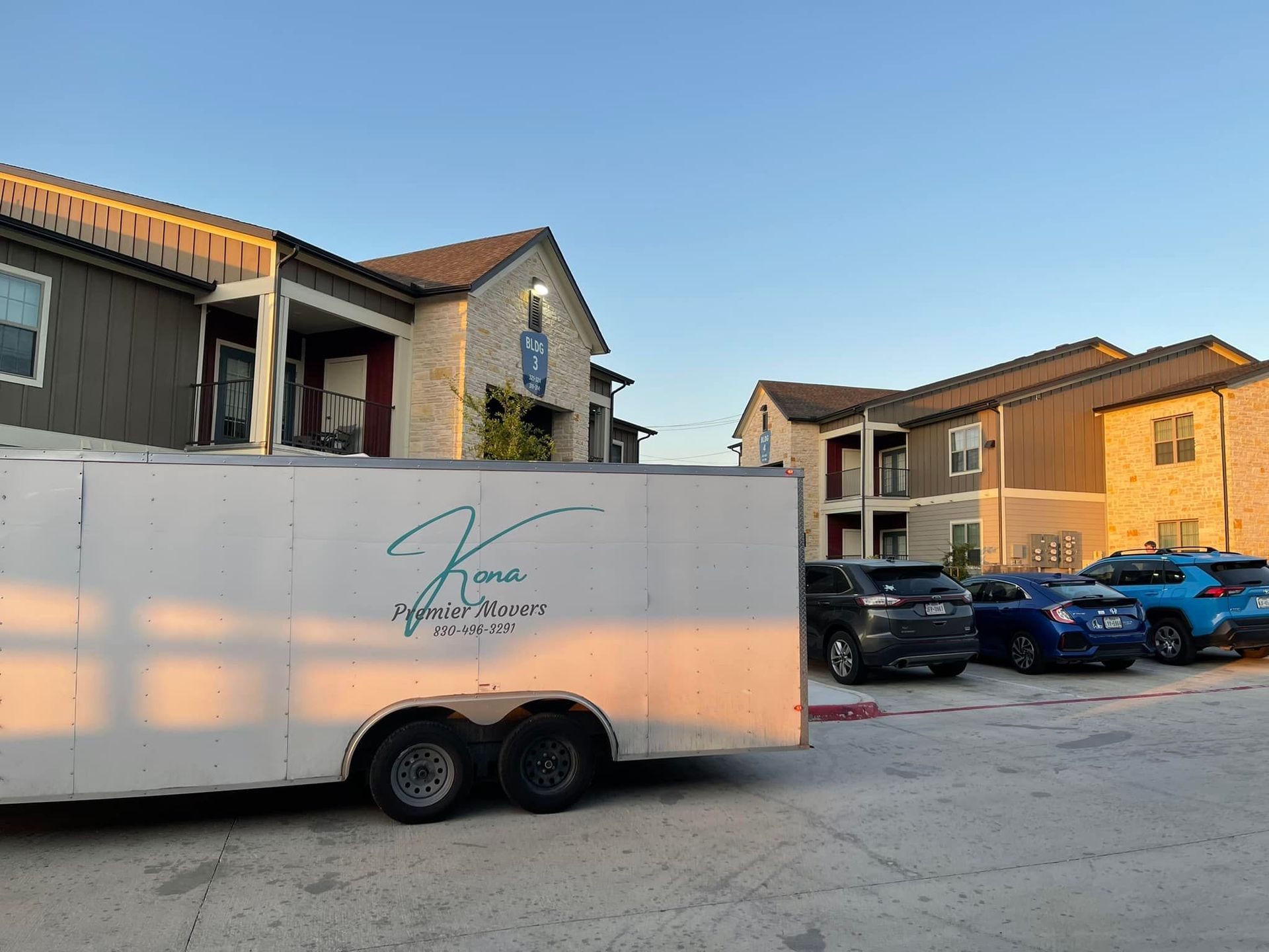 A white trailer with the letter k on it is parked in front of a building