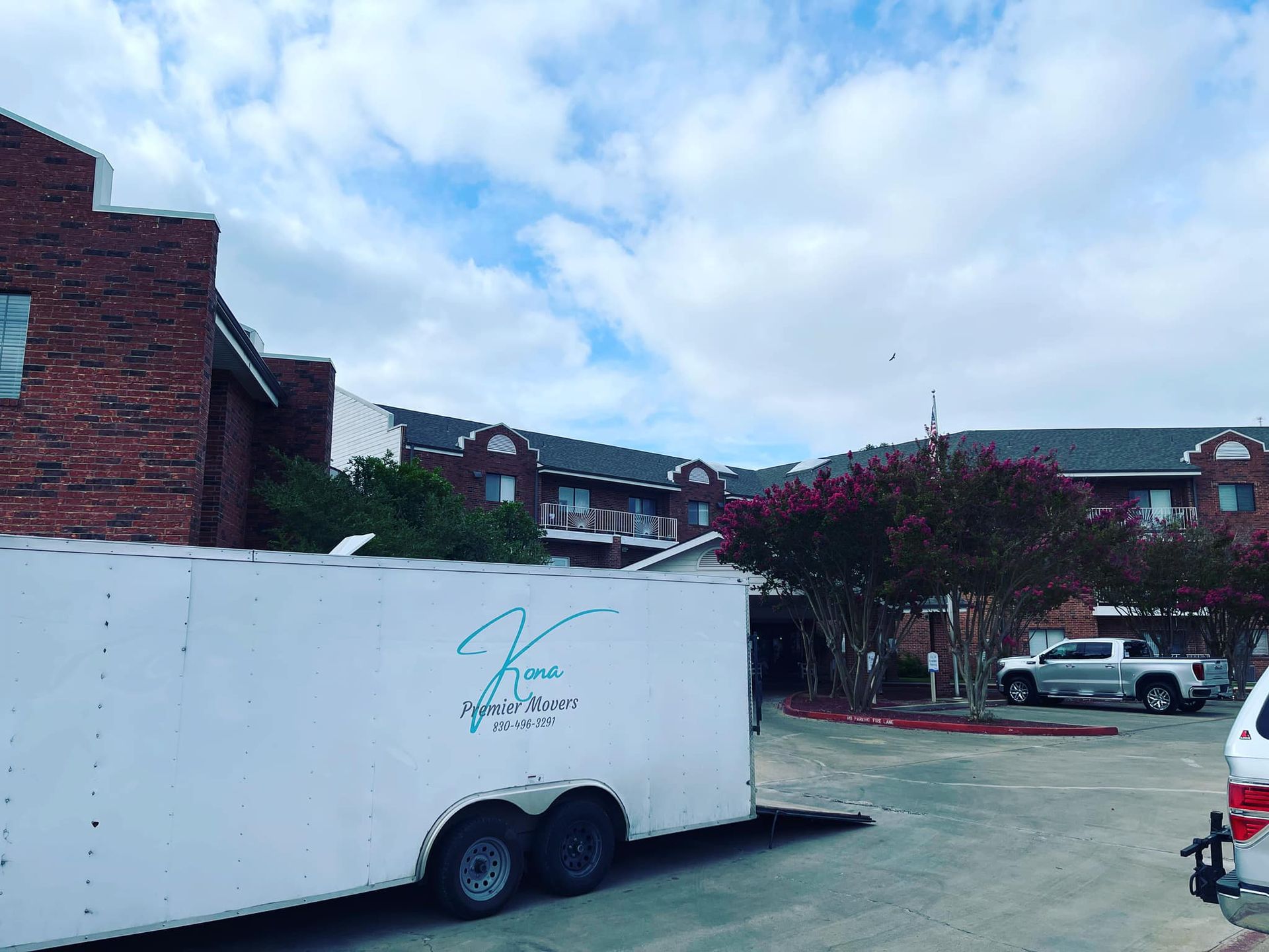 A white trailer is parked in front of a brick building.