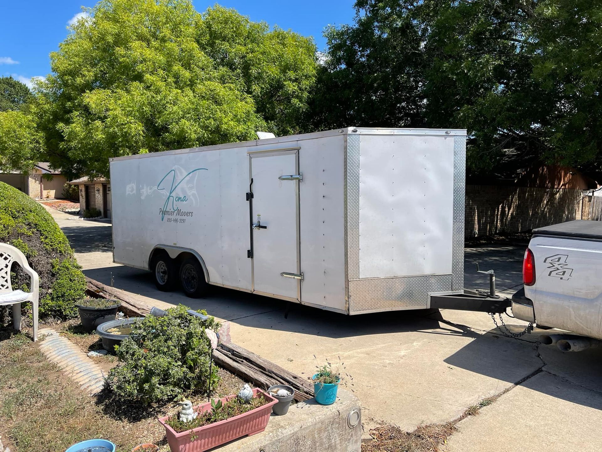 A white trailer is parked in a driveway next to a truck.