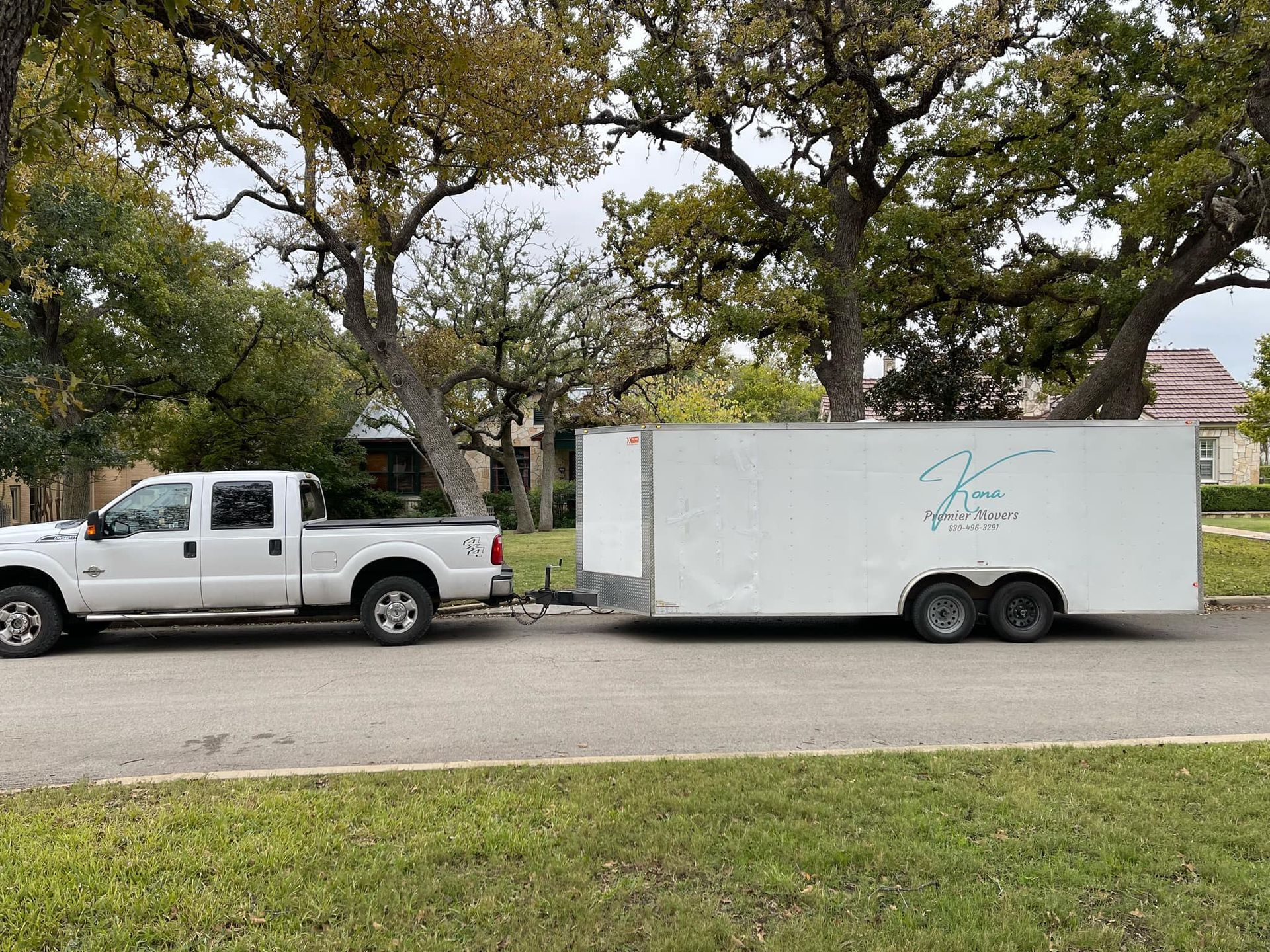 A white truck is towing a white trailer down a street.